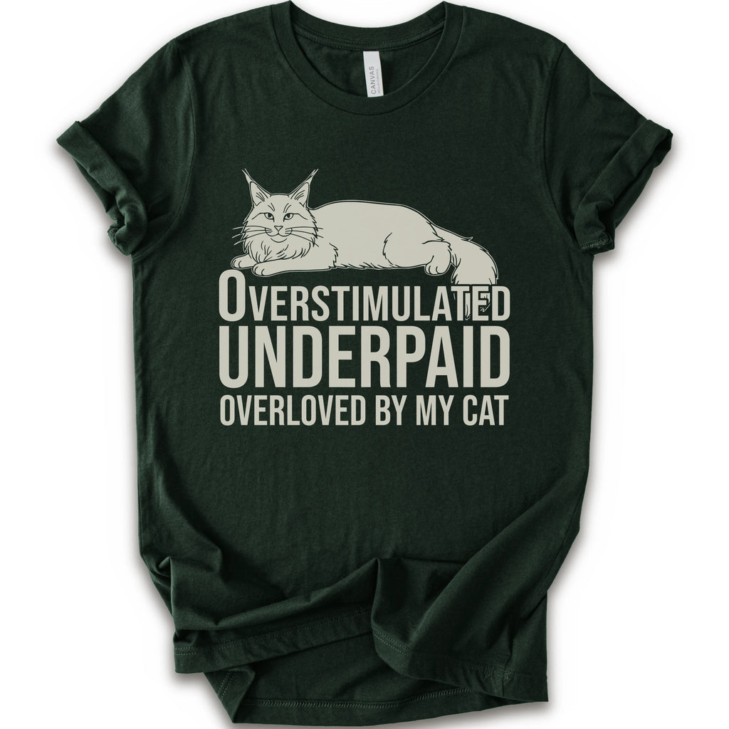 A forest short-sleeve crewneck T-shirt with a lounging cat graphic and “Overstimulated, Underpaid, Overloved by My Cat” text.