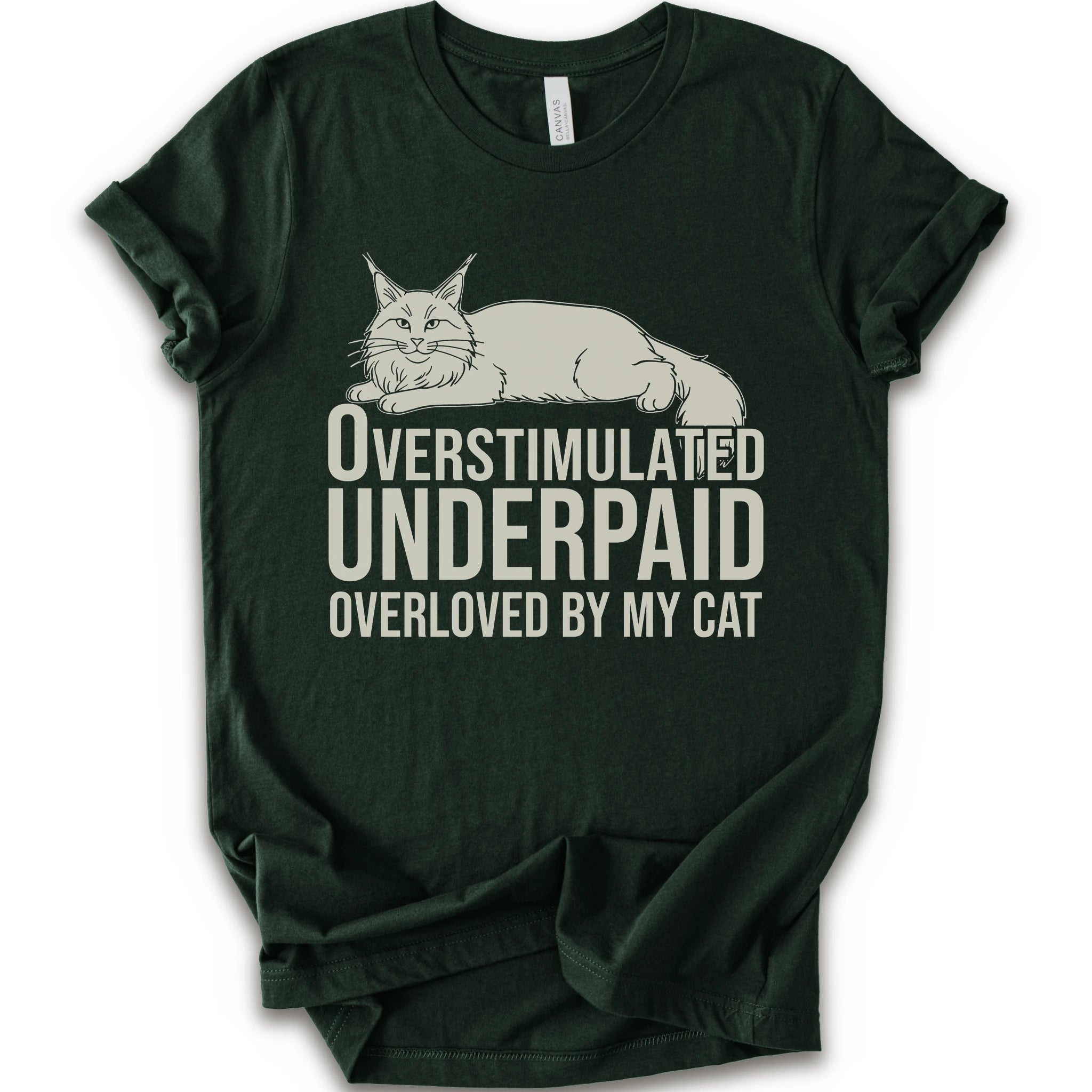 A forest short-sleeve crewneck T-shirt with a lounging cat graphic and “Overstimulated, Underpaid, Overloved by My Cat” text.