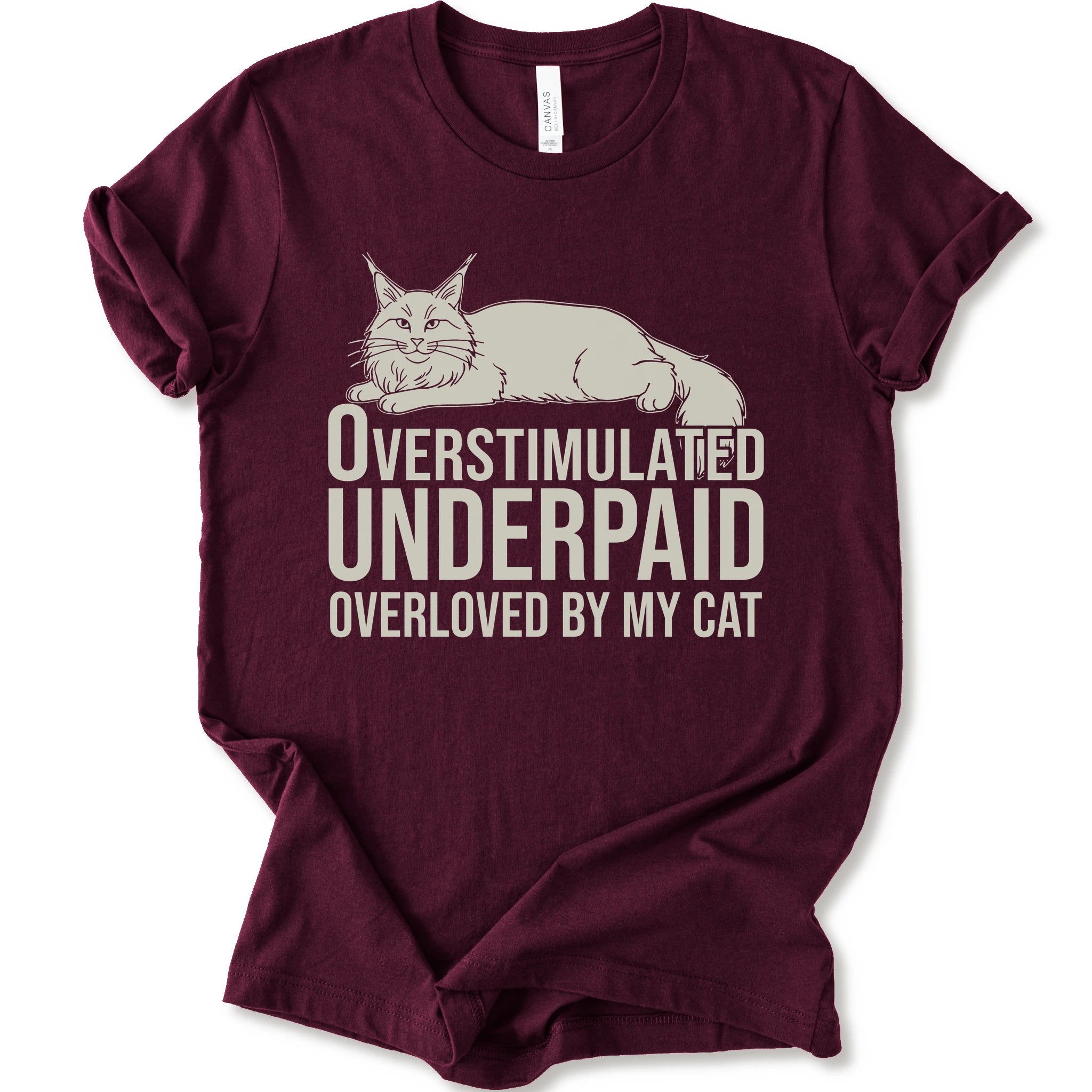A maroon short-sleeve crewneck T-shirt with a lounging cat graphic and “Overstimulated, Underpaid, Overloved by My Cat” text.