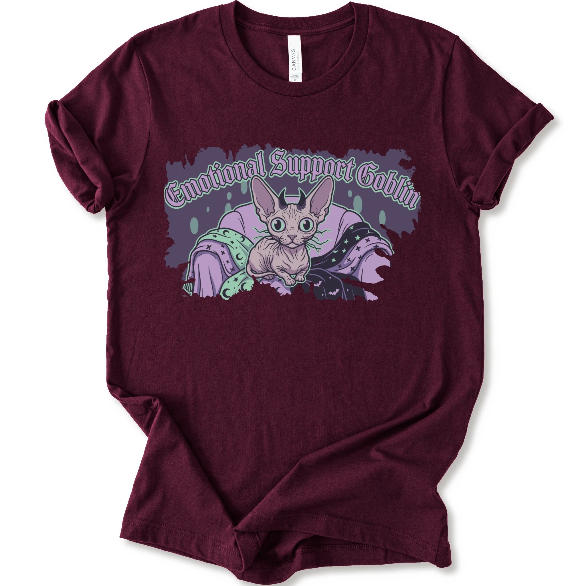 A maroon short-sleeve t-shirt with a graphic print of a cartoon sphynx cat in a purple blanket with the text 'Emotional Support Goblin'.