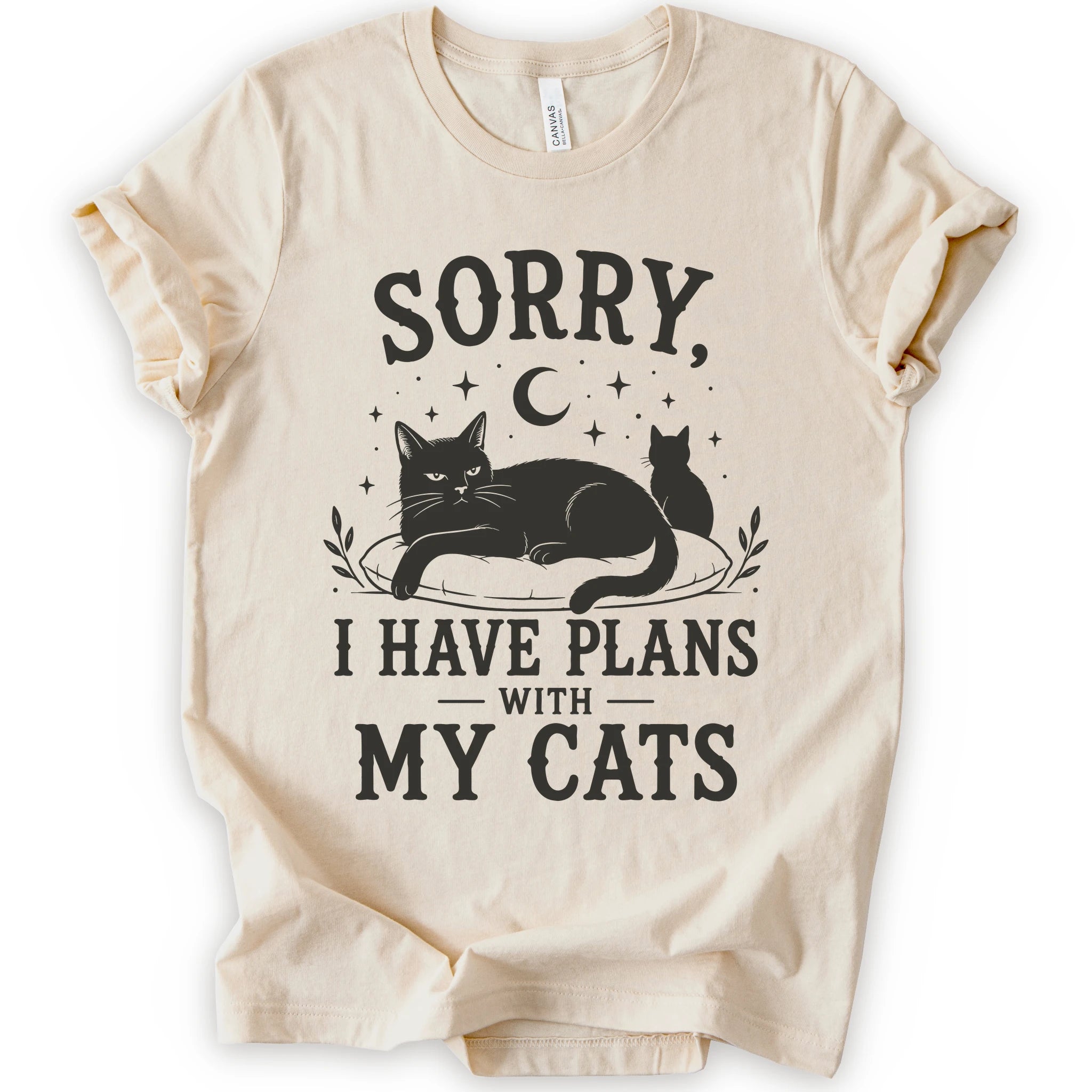 A natural short-sleeve t-shirt with a black graphic print of two cats, a crescent moon, and stars, accompanied by the text 'SORRY, I HAVE PLANS WITH MY CATS'.