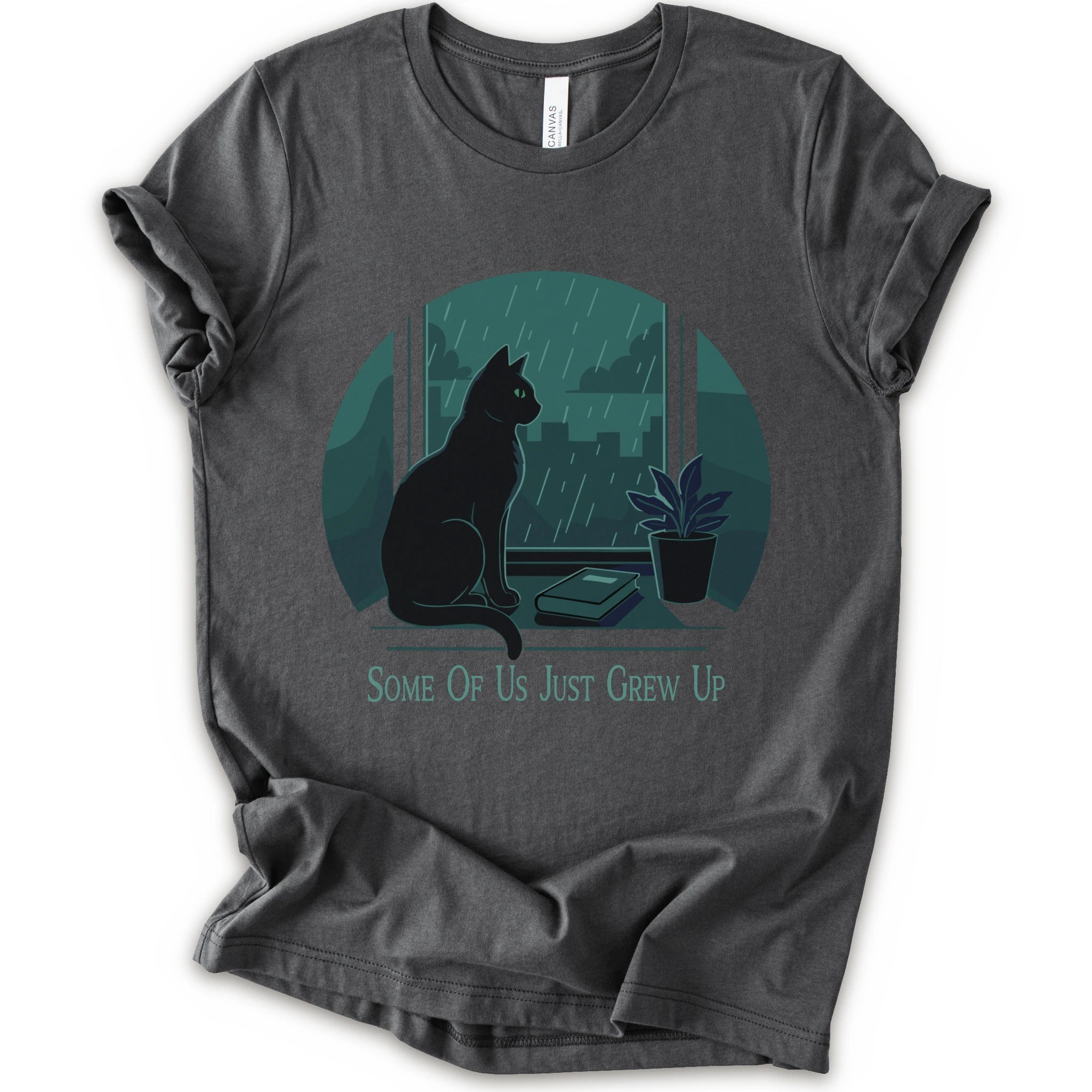 A asphalt short-sleeve crewneck t-shirt with a graphic print of a black cat sitting by a window in the rain, next to a small potted plant, with the text 'SOME OF US JUST GREW UP' printed below.