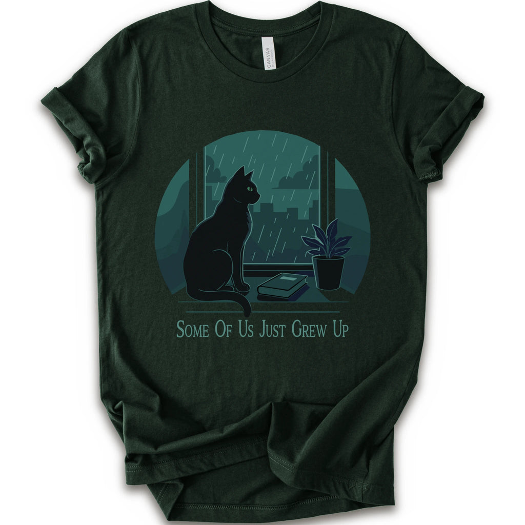 A forest short-sleeve crewneck t-shirt with a graphic print of a black cat sitting by a window in the rain, next to a small potted plant, with the text 'SOME OF US JUST GREW UP' printed below.