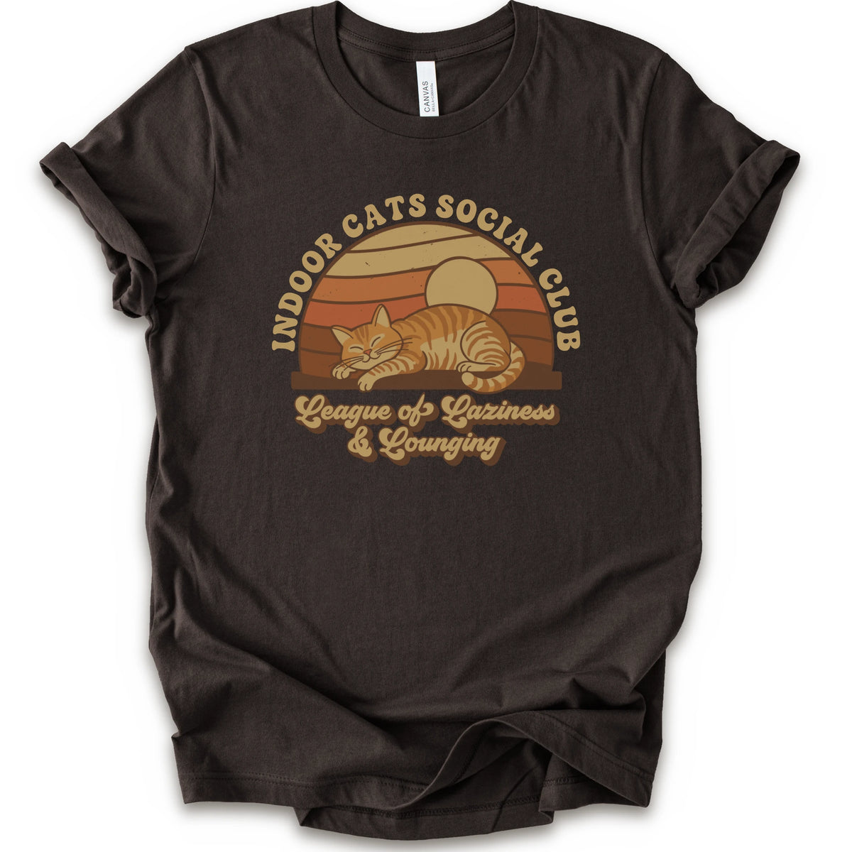 A brown short-sleeve crewneck t-shirt featuring a retro-style graphic of an orange tabby cat sleeping under a sunset, with the text 'INDOOR CATS SOCIAL CLUB' and 'League of Laziness & Lounging'.