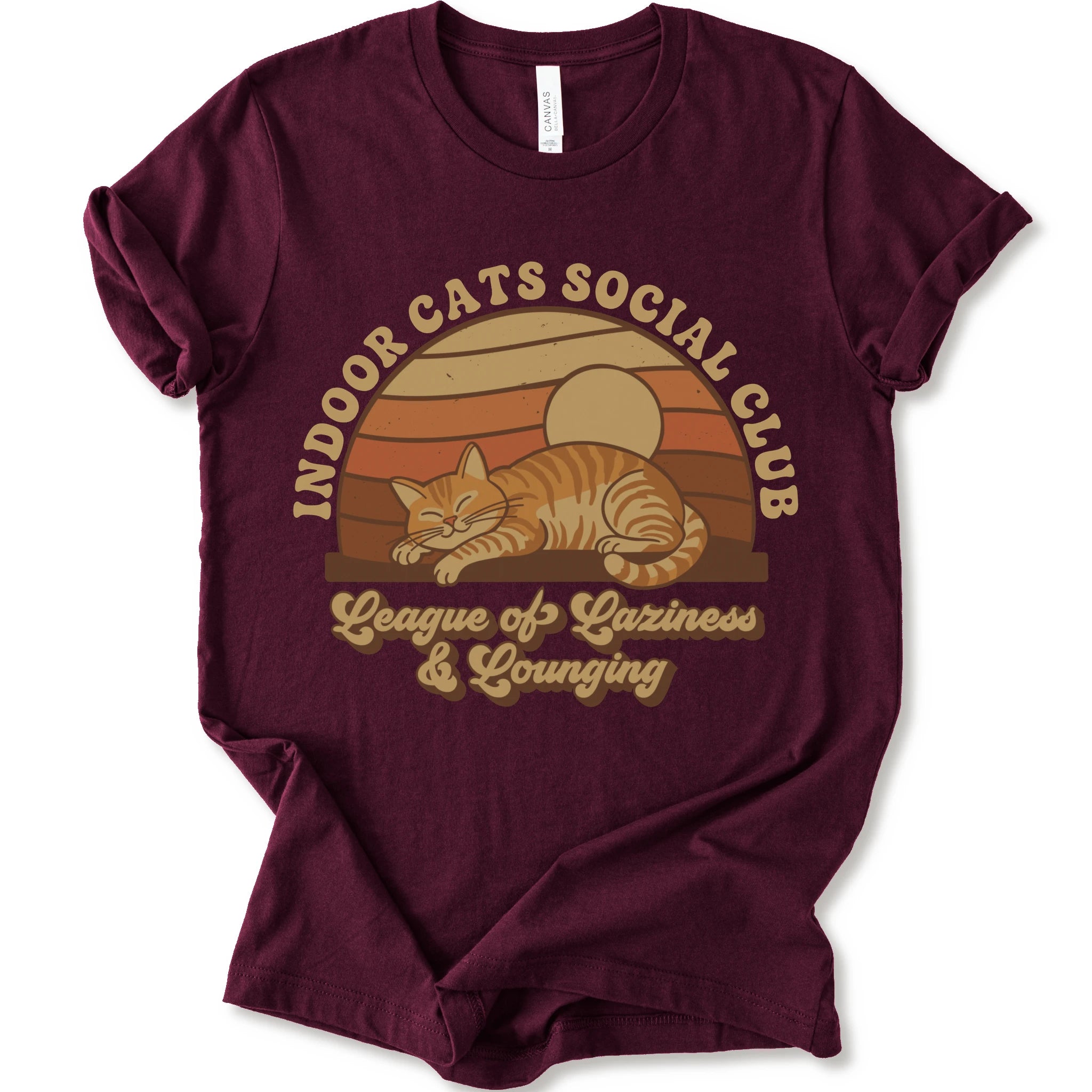 A maroon short-sleeve crewneck t-shirt with a retro-style graphic of an orange tabby cat sleeping under a sunset, with the text 'INDOOR CATS SOCIAL CLUB' and 'League of Laziness & Younging'.