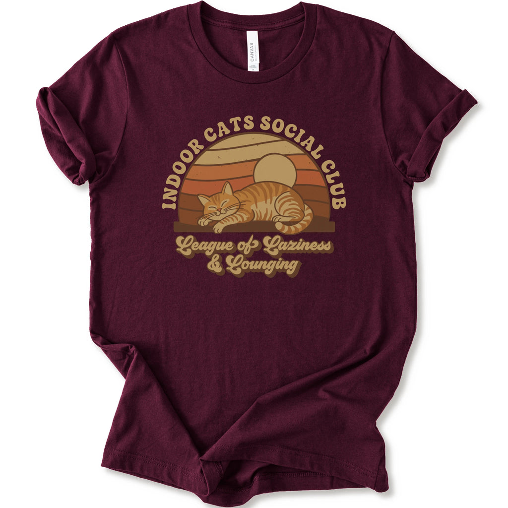 A maroon short-sleeve crewneck t-shirt featuring a retro-style graphic of an orange tabby cat sleeping under a sunset, with the text 'INDOOR CATS SOCIAL CLUB' and 'League of Laziness & Lounging'.