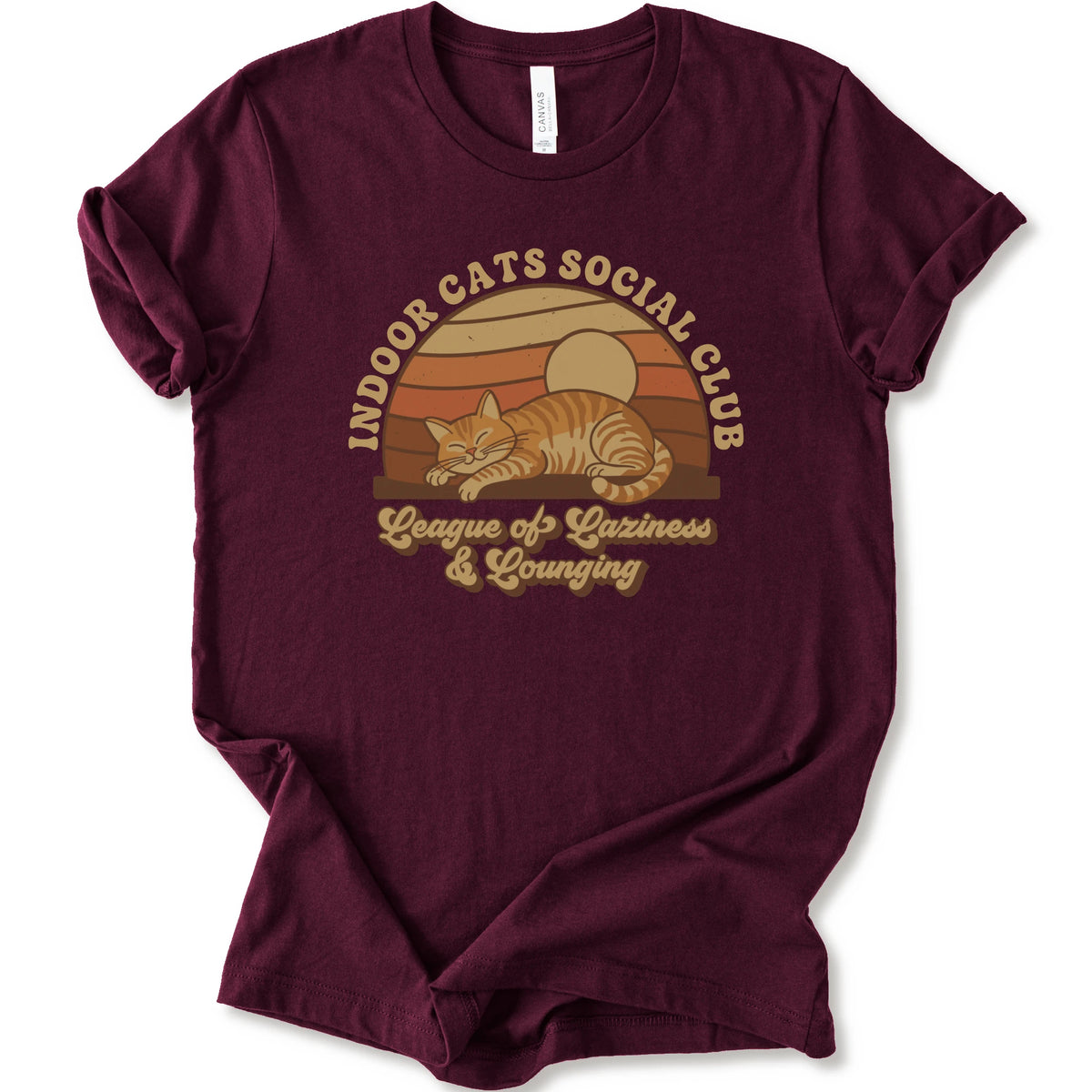 A maroon short-sleeve crewneck t-shirt featuring a retro-style graphic of an orange tabby cat sleeping under a sunset, with the text 'INDOOR CATS SOCIAL CLUB' and 'League of Laziness & Lounging'.
