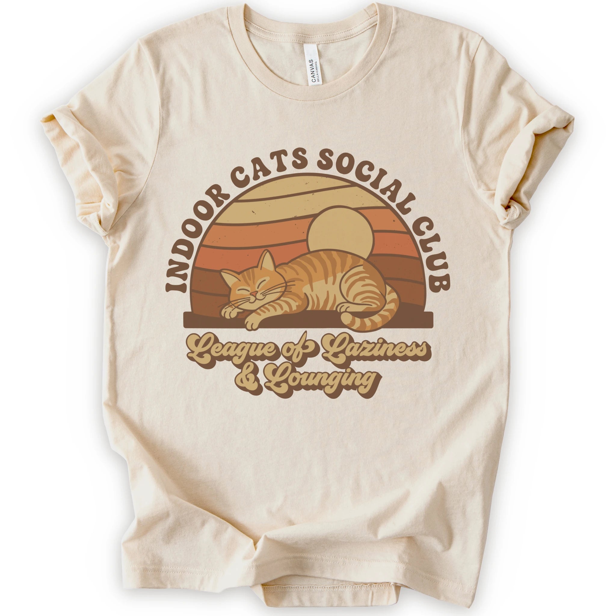 A natural short-sleeve crewneck t-shirt with a retro-style graphic of an orange tabby cat sleeping under a sunset, with the text 'INDOOR CATS SOCIAL CLUB' and 'League of Laziness & Younging'.