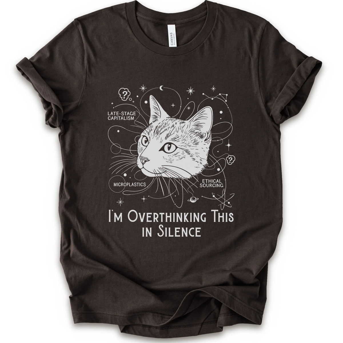 A brown short-sleeve crewneck t-shirt with a white graphic print of a cat's head surrounded by celestial and philosophical doodles, with the text 'I'M OVERTHINKING THIS IN SILENCE'.