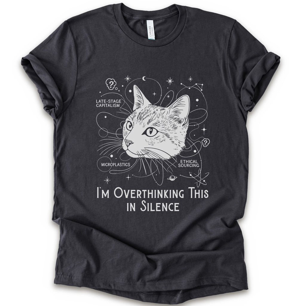 A dark grey short-sleeve crewneck t-shirt with a white graphic print of a cat's head surrounded by celestial and philosophical doodles, with the text 'I'M OVERTHINKING THIS IN SILENCE'.