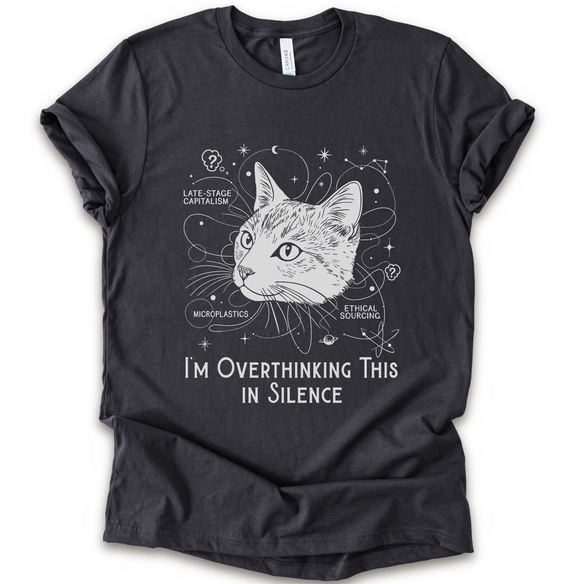 A dark grey short-sleeve crewneck t-shirt with a white graphic print of a cat's head surrounded by celestial and philosophical doodles, with the text 'I'M OVERTHINKING THIS IN SILENCE'.
