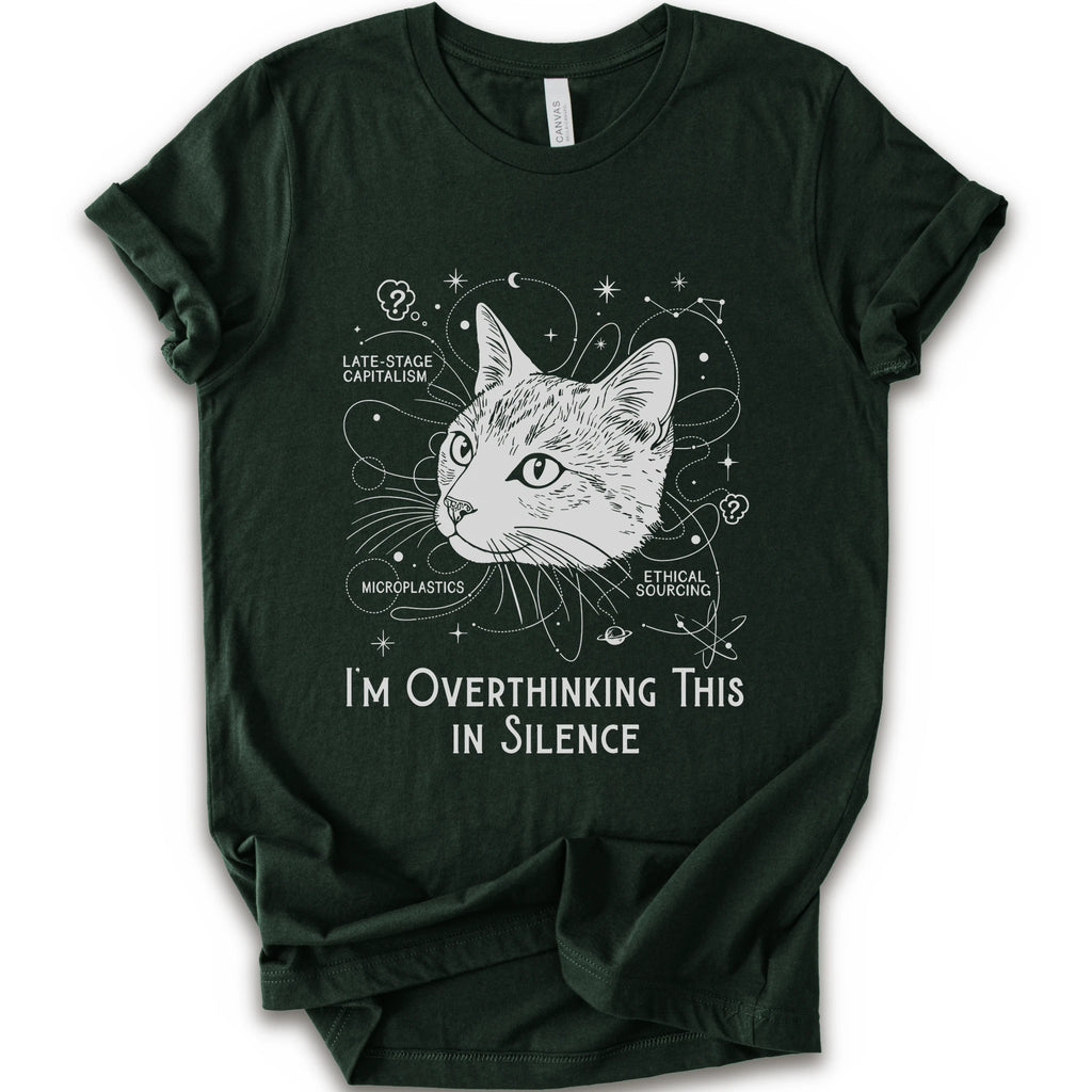 A forest short-sleeve crewneck t-shirt with a white graphic print of a cat's head surrounded by celestial and philosophical doodles, with the text 'I'M OVERTHINKING THIS IN SILENCE'.