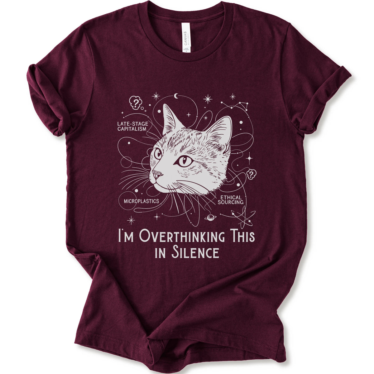 A maroon short-sleeve crewneck t-shirt with a white graphic print of a cat's head surrounded by celestial and philosophical doodles, with the text 'I'M OVERTHINKING THIS IN SILENCE'.