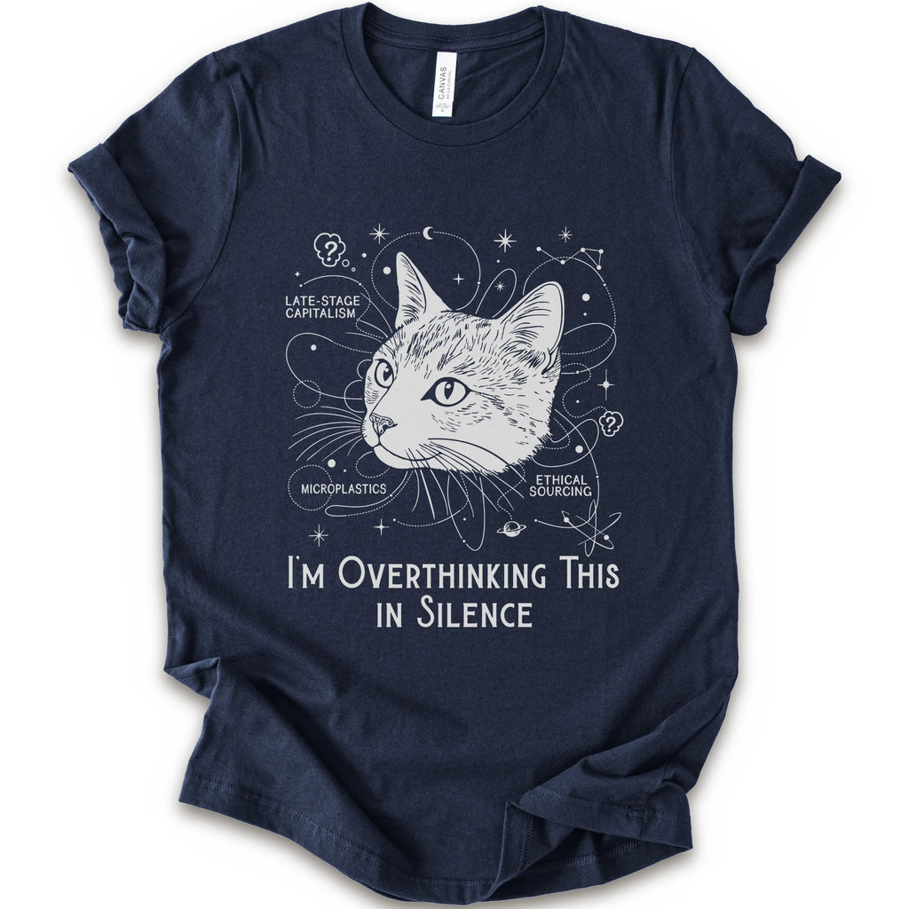 A navy short-sleeve crewneck t-shirt with a white graphic print of a cat's head surrounded by celestial and philosophical doodles, with the text 'I'M OVERTHINKING THIS IN SILENCE'.