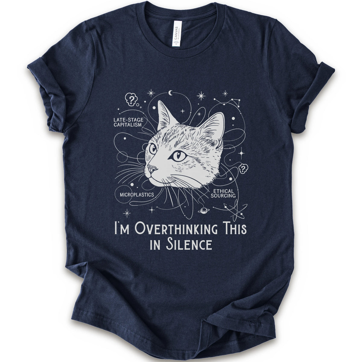 A navy short-sleeve crewneck t-shirt with a white graphic print of a cat's head surrounded by celestial and philosophical doodles, with the text 'I'M OVERTHINKING THIS IN SILENCE'.