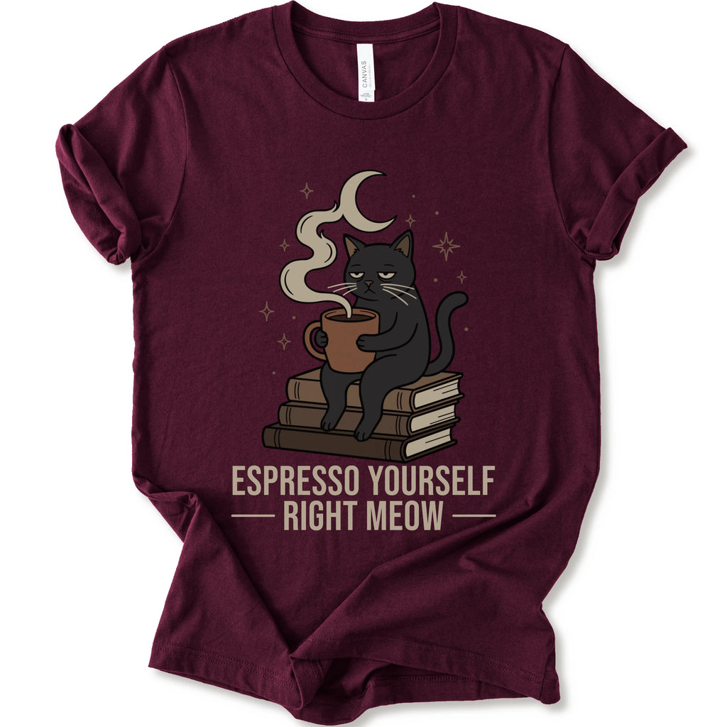 A maroon short-sleeve crewneck t-shirt featuring a graphic of a black cat sitting on books and holding an espresso cup, with a crescent moon and stars above. The text 'ESPRESSO YOURSELF RIGHT MEOW' is printed below in beige.