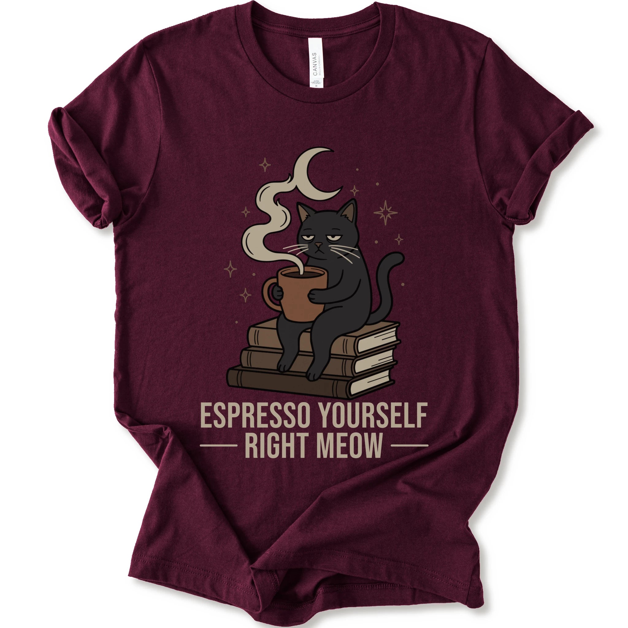 A maroon short-sleeve crewneck t-shirt featuring a graphic of a black cat sitting on books and holding an espresso cup, with a crescent moon and stars above. The text 'ESPRESSO YOURSELF RIGHT MEOW' is printed below in beige.