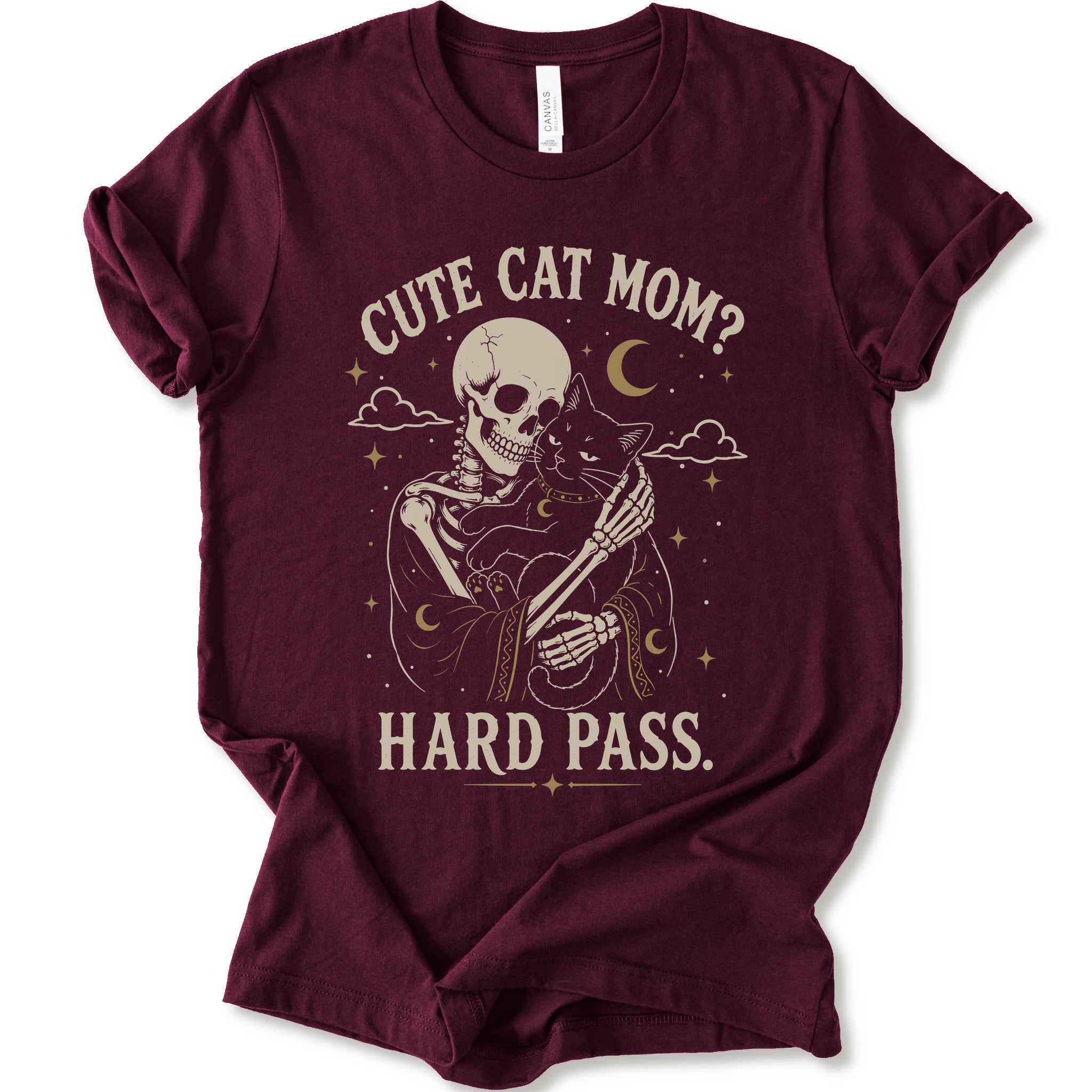 A maroon short-sleeve crewneck t-shirt with a vintage-style graphic of a skeleton cat holding a black cat under the text 'CUTE CAT MOM? HARD PASS.' in a distressed cream color.