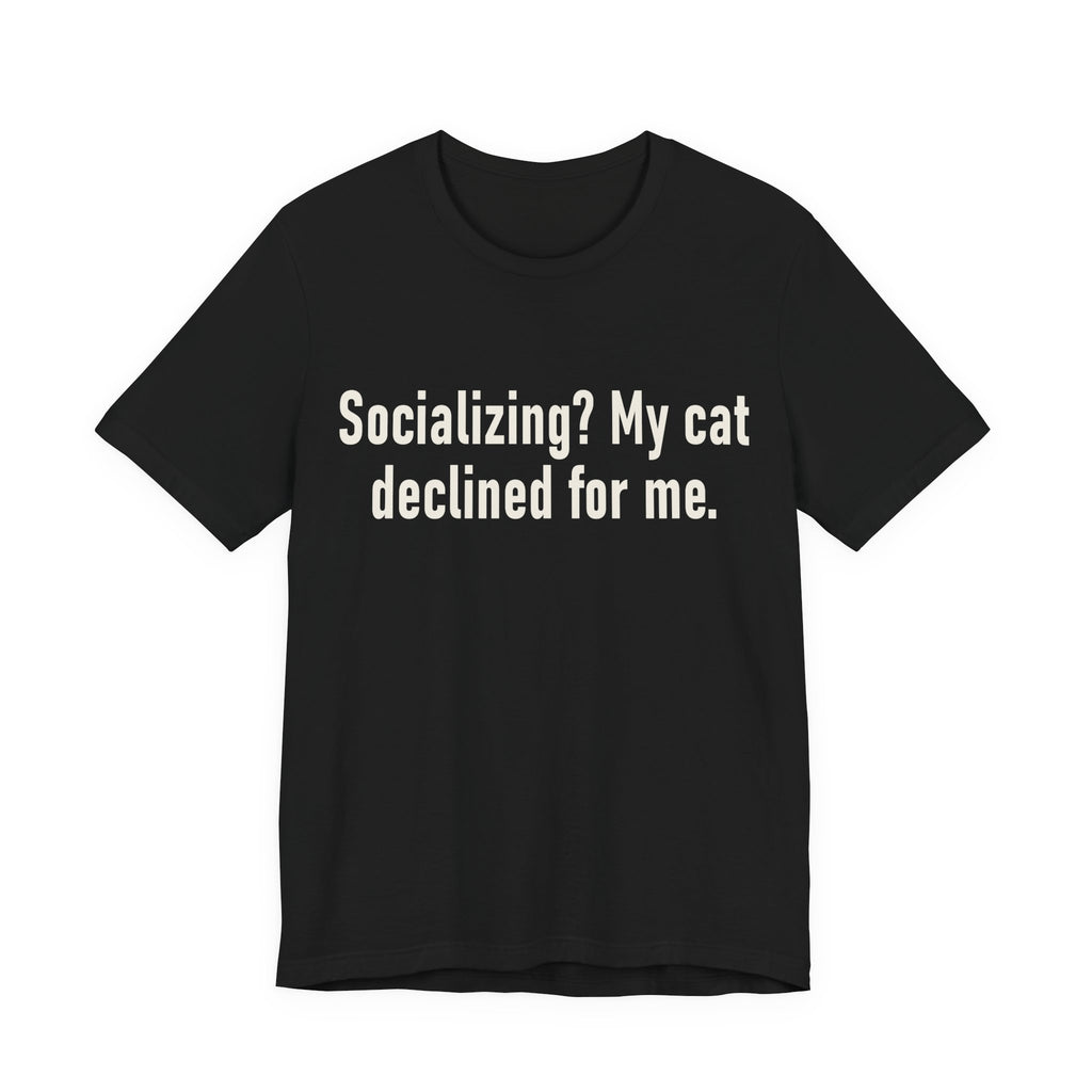 A black short-sleeve crewneck t-shirt featuring a graphic with large cream-colored text reads “Socializing? My cat declined for me.” across two centered lines. The design is minimal, high-contrast and entirely typographic.