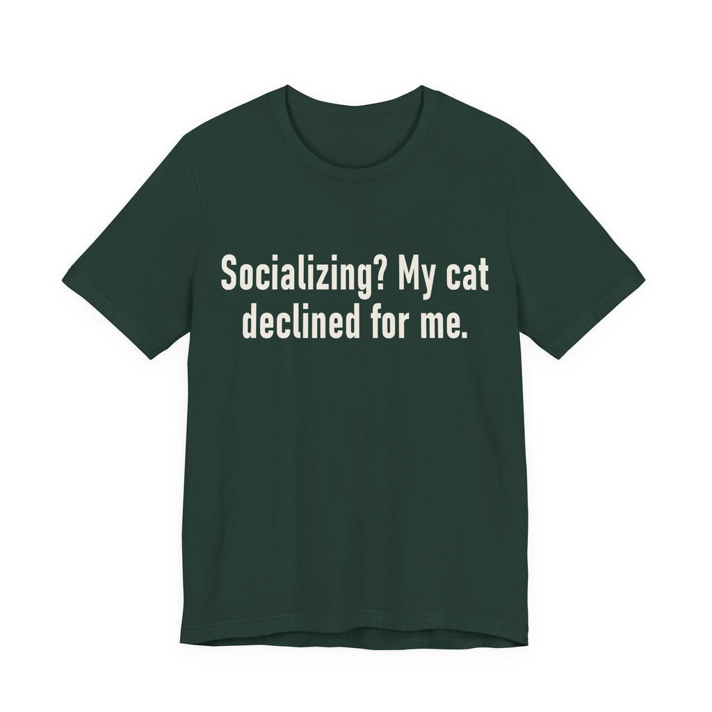 A forest short-sleeve crewneck t-shirt featuring a graphic with large cream-colored text reads “Socializing? My cat declined for me.” across two centered lines. The design is minimal, high-contrast and entirely typographic.