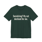 A forest short-sleeve crewneck t-shirt featuring a graphic with large cream-colored text reads “Socializing? My cat declined for me.” across two centered lines. The design is minimal, high-contrast and entirely typographic.