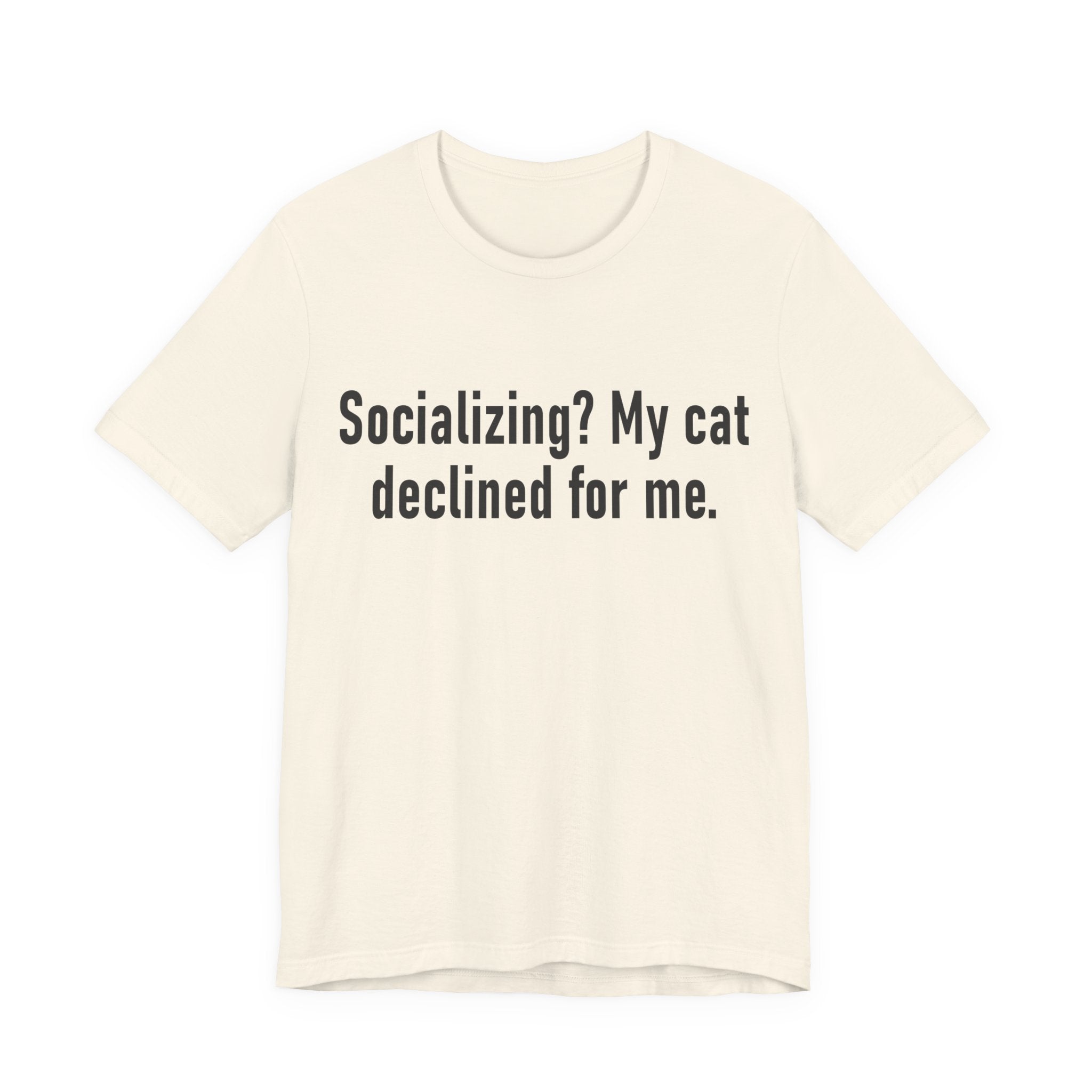 A natural short-sleeve crewneck t-shirt featuring a graphic with large black-colored text reads “Socializing? My cat declined for me.” across two centered lines. The design is minimal, high-contrast and entirely typographic.
