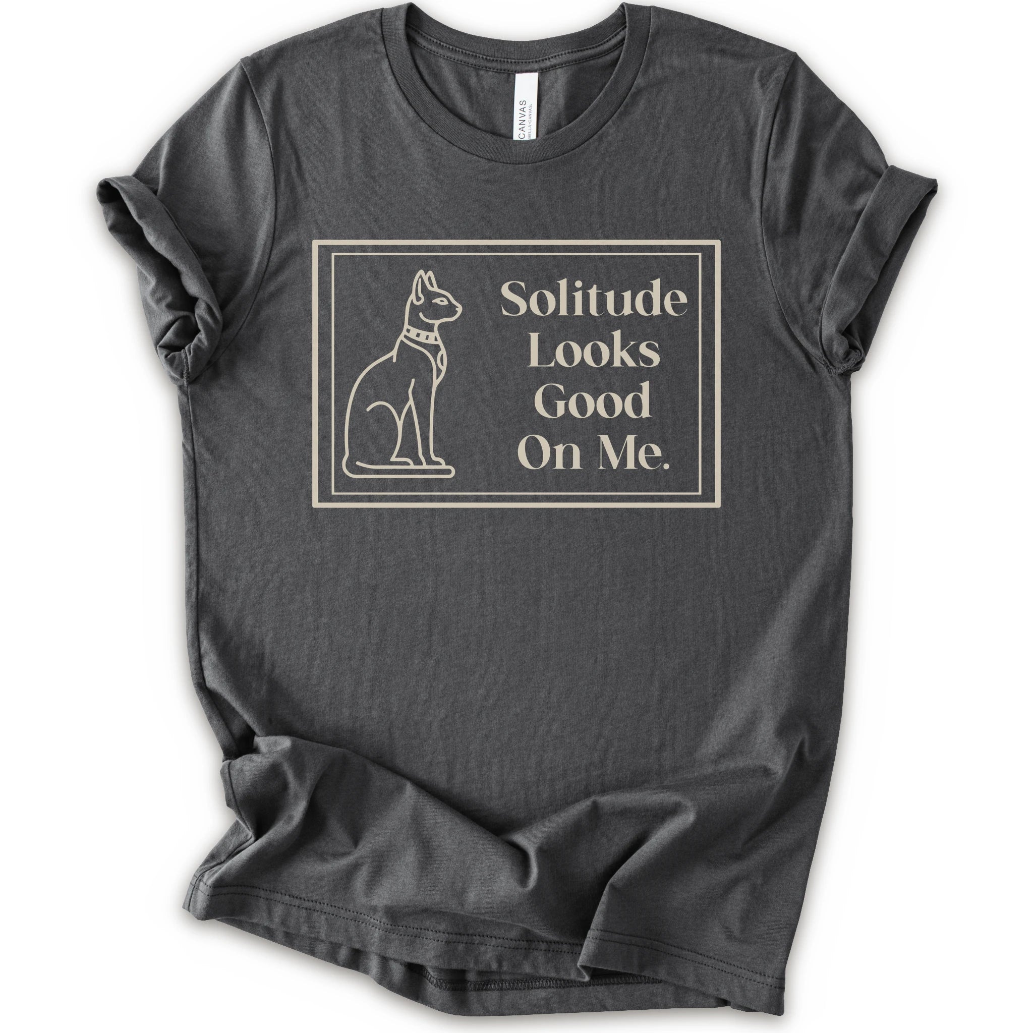 A asphalt short-sleeve crewneck t-shirt with a cream-colored graphic on the front, features a thin rectangular border enclosing a line-art illustration of a cat on the left and the text 'Solitude Looks Good On Me.