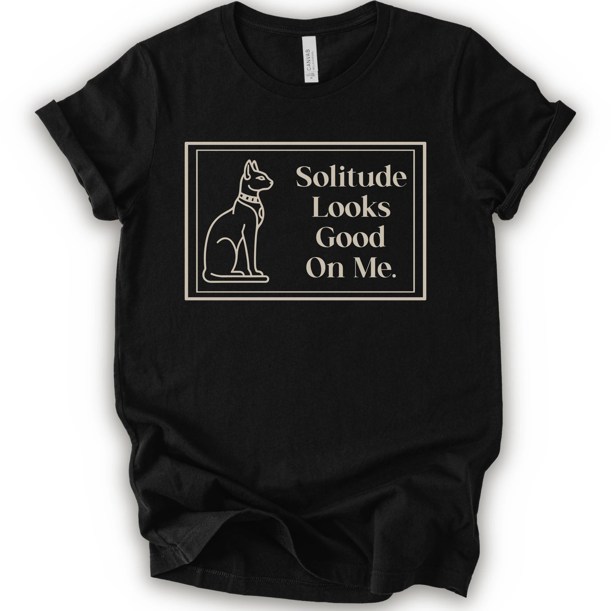 A black short-sleeve crewneck t-shirt with a cream-colored graphic on the front, features a thin rectangular border enclosing a line-art illustration of a cat on the left and the text 'Solitude Looks Good On Me.