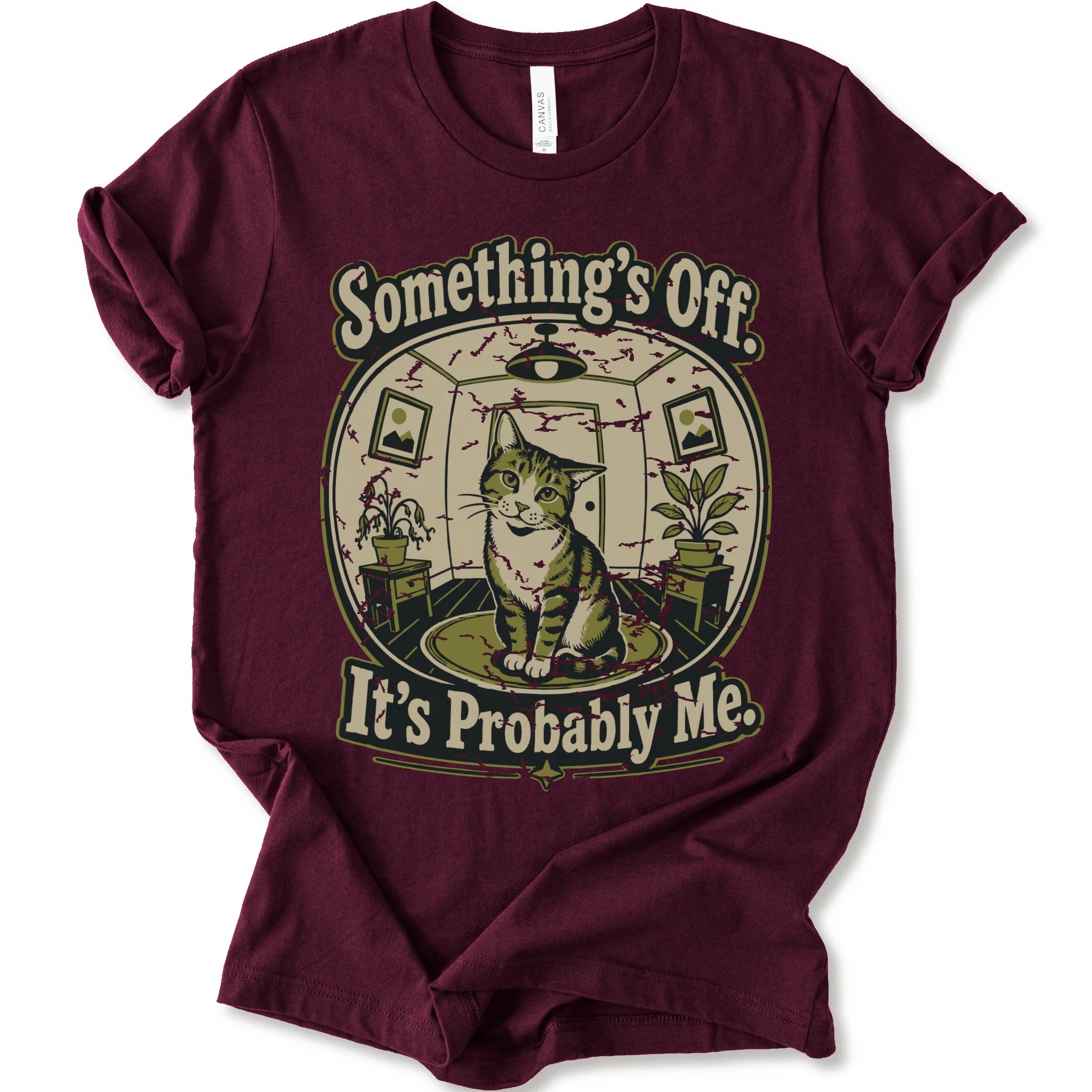 A maroon short-sleeve crewneck t-shirt with a vintage-style graphic of a cat in a hat inside a circular room, with the text 'Something's Off. It's Probably Me.