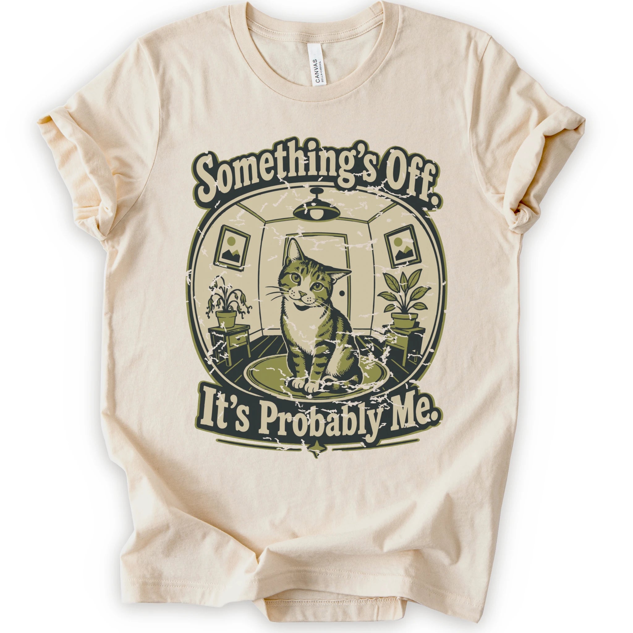 A natural short-sleeve crewneck t-shirt with a vintage-style graphic of a cat in a hat inside a circular room, with the text 'Something's Off. It's Probably Me.