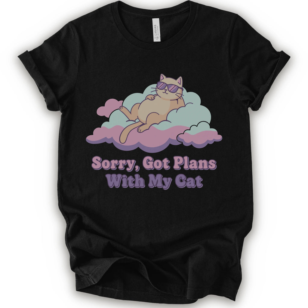A black short-sleeve t-shirt with a graphic of a sleeping orange cat wearing sunglasses on pink and light blue clouds, with the text 'Sorry, Got Plans With My Cat'.
