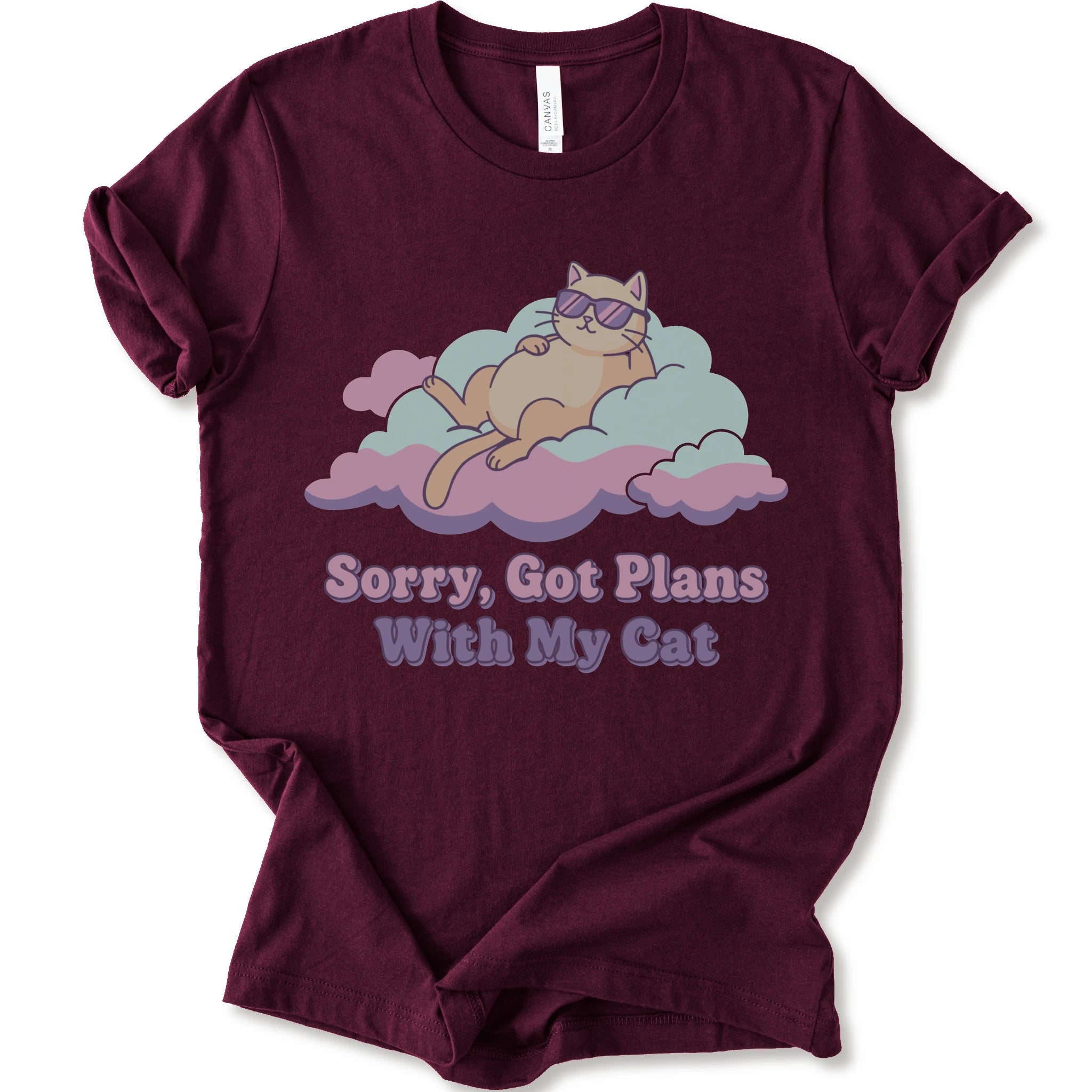 A maroon short-sleeve t-shirt with a graphic of a sleeping orange cat wearing sunglasses on pink and light blue clouds, with the text 'Sorry, Got Plans With My Cat'.