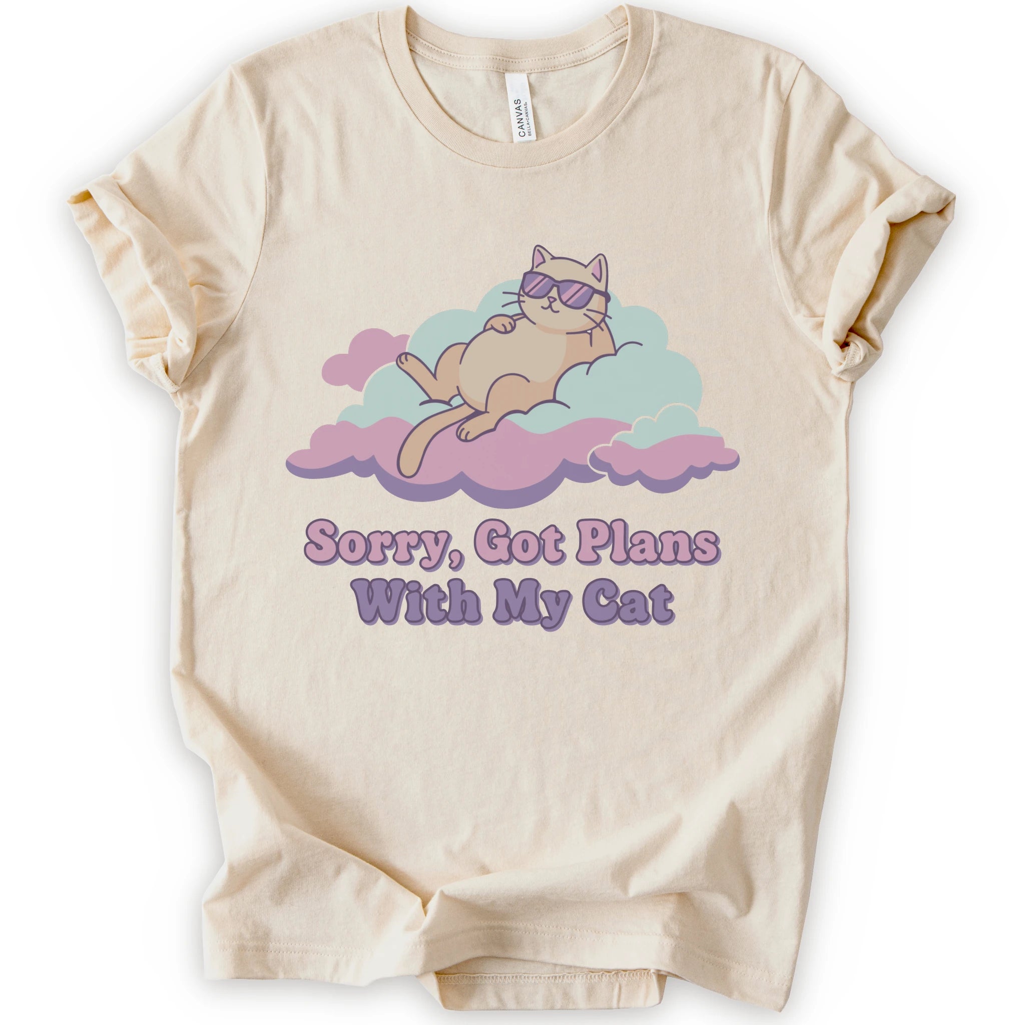 A natural short-sleeve t-shirt with a graphic of a sleeping orange cat wearing sunglasses on pink and light blue clouds, with the text 'Sorry, Got Plans With My Cat'.