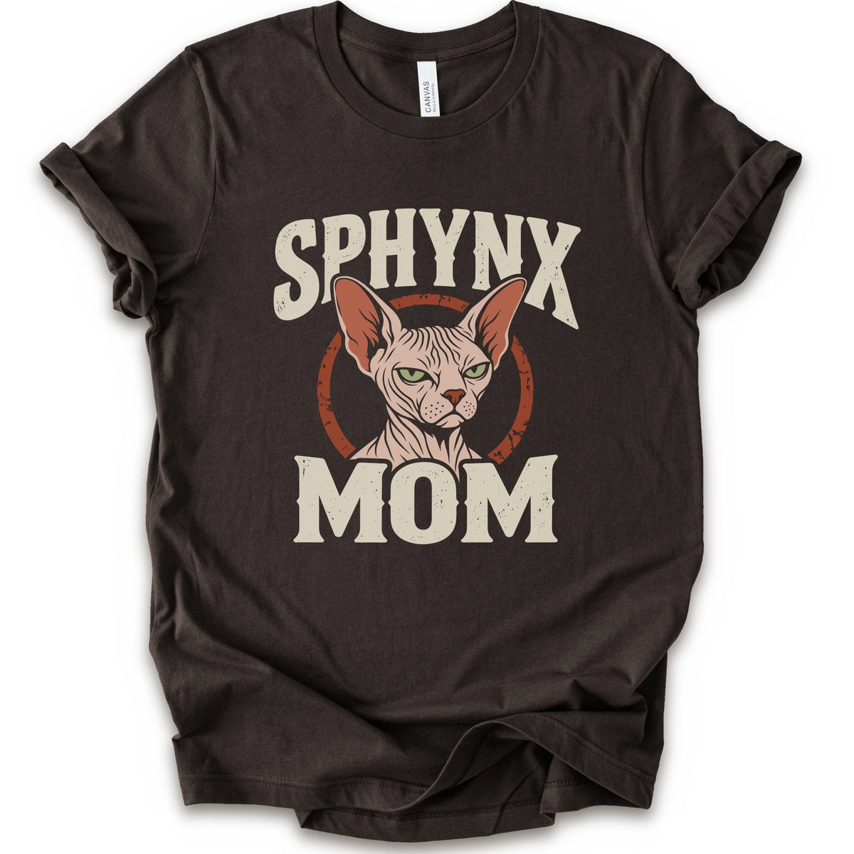 A brown short-sleeve crewneck t-shirt with a graphic print of a Sphynx cat and the text 'SPHYNX MOM' in distressed cream lettering.