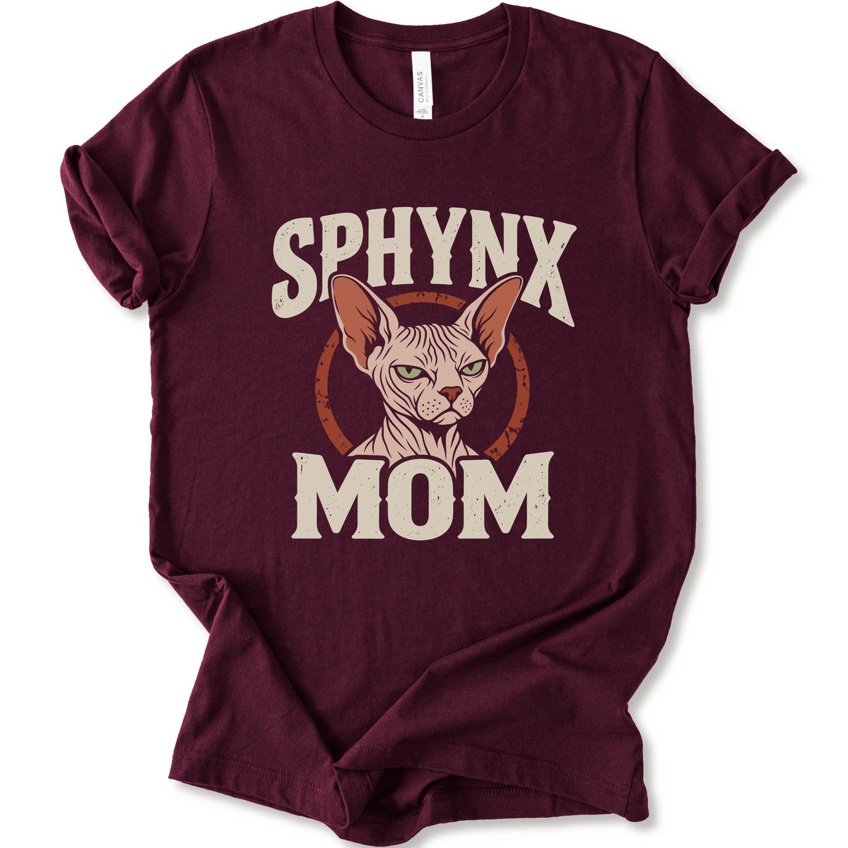 A maroon short-sleeve crewneck t-shirt with a graphic print of a Sphynx cat and the text 'SPHYNX MOM' in distressed cream lettering.