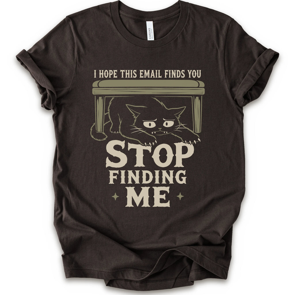 Brown graphic t-shirt with a black cat crouching under a desk with “I Hope This Email Finds You” and “Stop Finding Me” distressed text