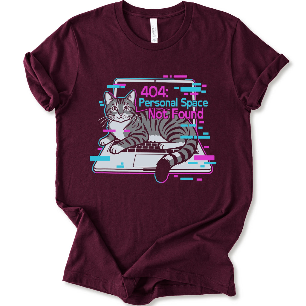 A maroon short-sleeve crewneck t-shirt with a graphic print of a gray tabby cat sitting in front of a laptop displaying a '404: Personal Space Not Found' error message in pink and cyan text.