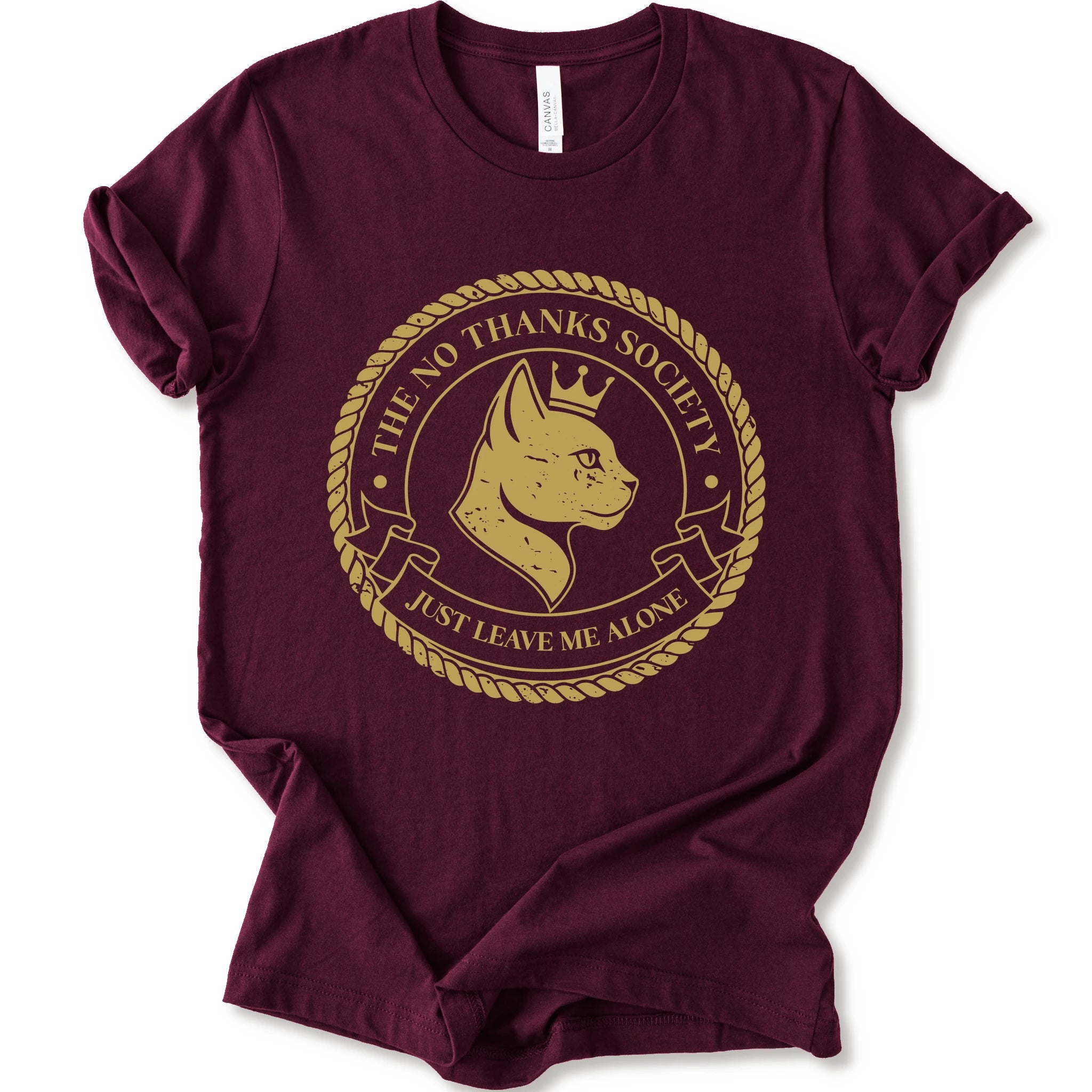 A maroon short-sleeve t-shirt with a circular graphic print on the front. The graphic features a golden-yellow cat profile wearing a crown, surrounded by a rope border and the text 'THE NO THANKS SOCIETY' and 'JUST LEAVE ME ALONE'.
