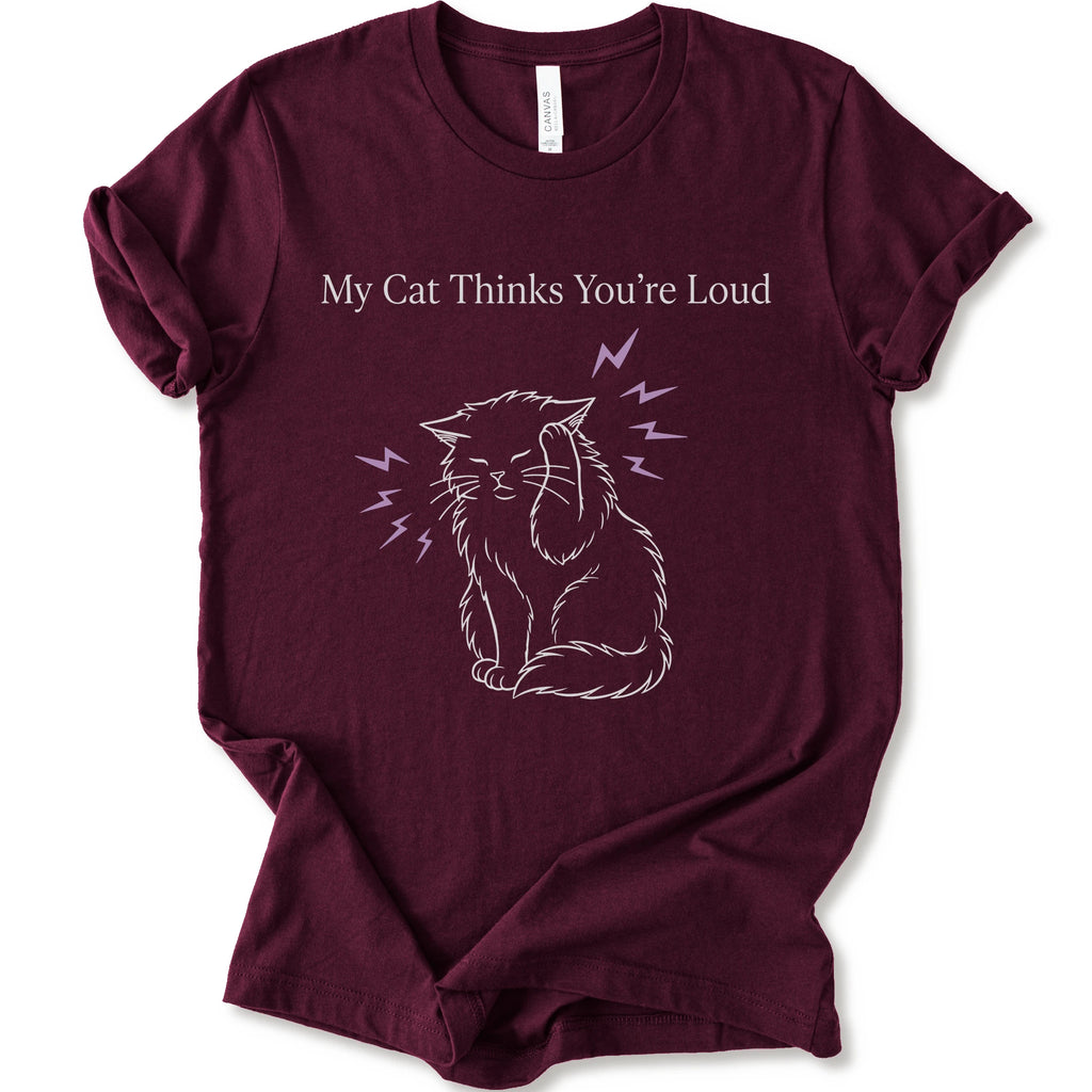 A maroon short-sleeve t-shirt with a graphic print of a white line-art cat closing its ear, surrounded by purple lightning bolts, with the text 'My Cat Thinks You're Loud' printed above in white.