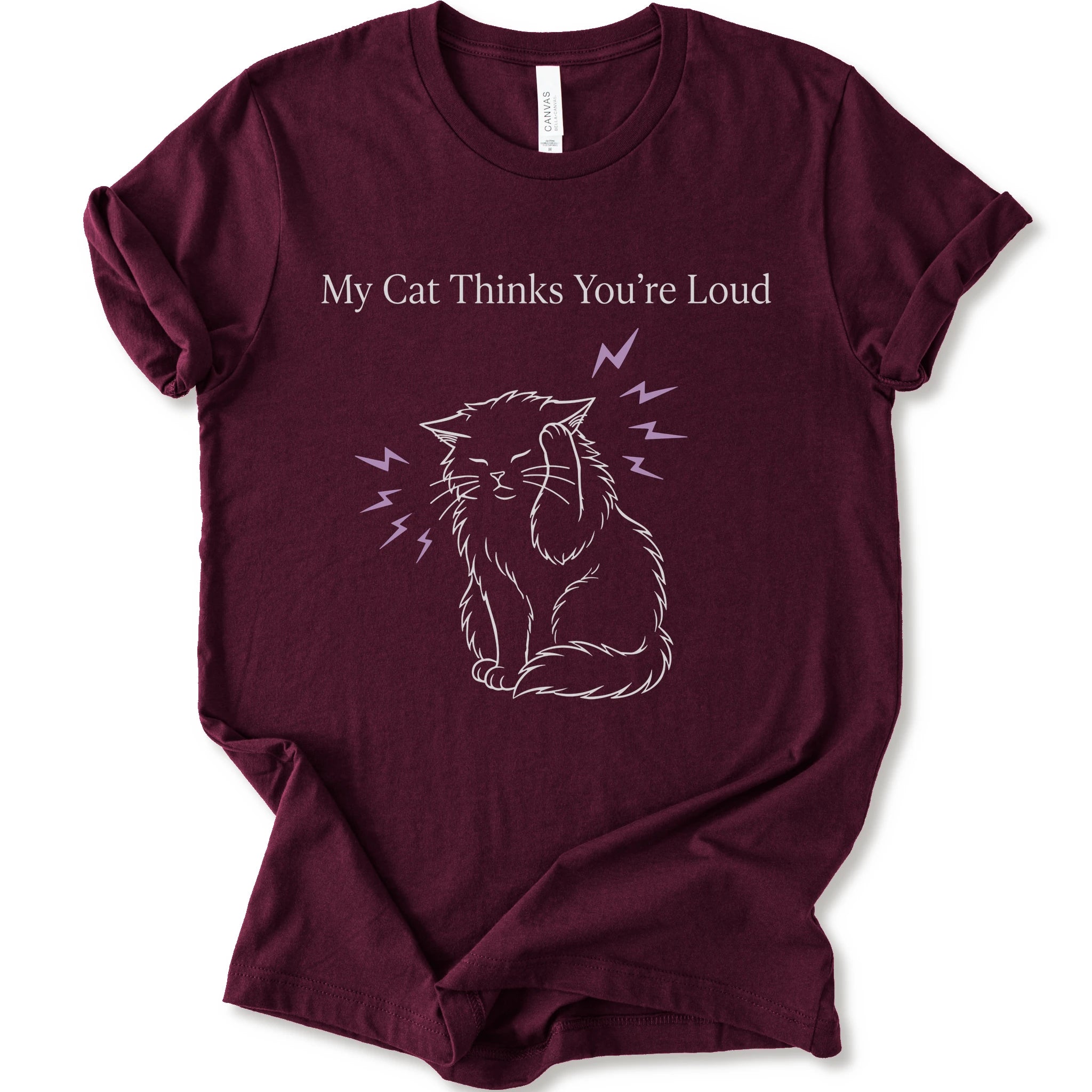 A maroon short-sleeve t-shirt with a graphic print of a white line-art cat closing its ear, surrounded by purple lightning bolts, with the text 'My Cat Thinks You're Loud' printed above in white.