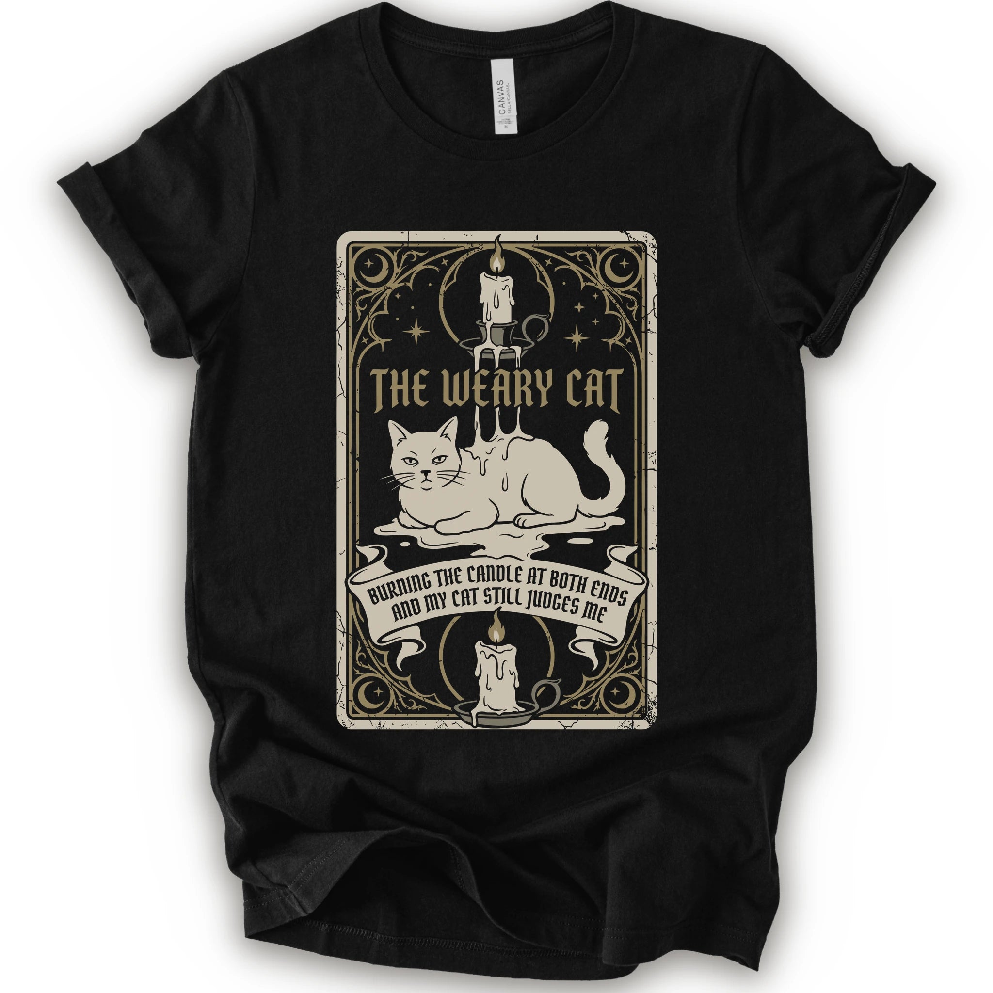 A black short-sleeve crewneck t-shirt with a vintage-style graphic print on the front. The print features a white cat lying down inside a decorative frame with candles, stars, and the text 'THE WEARY CAT' and 'BURNING THE CANDLE AT BOTH ENDS AND MY CAT STILL JUDGES ME.