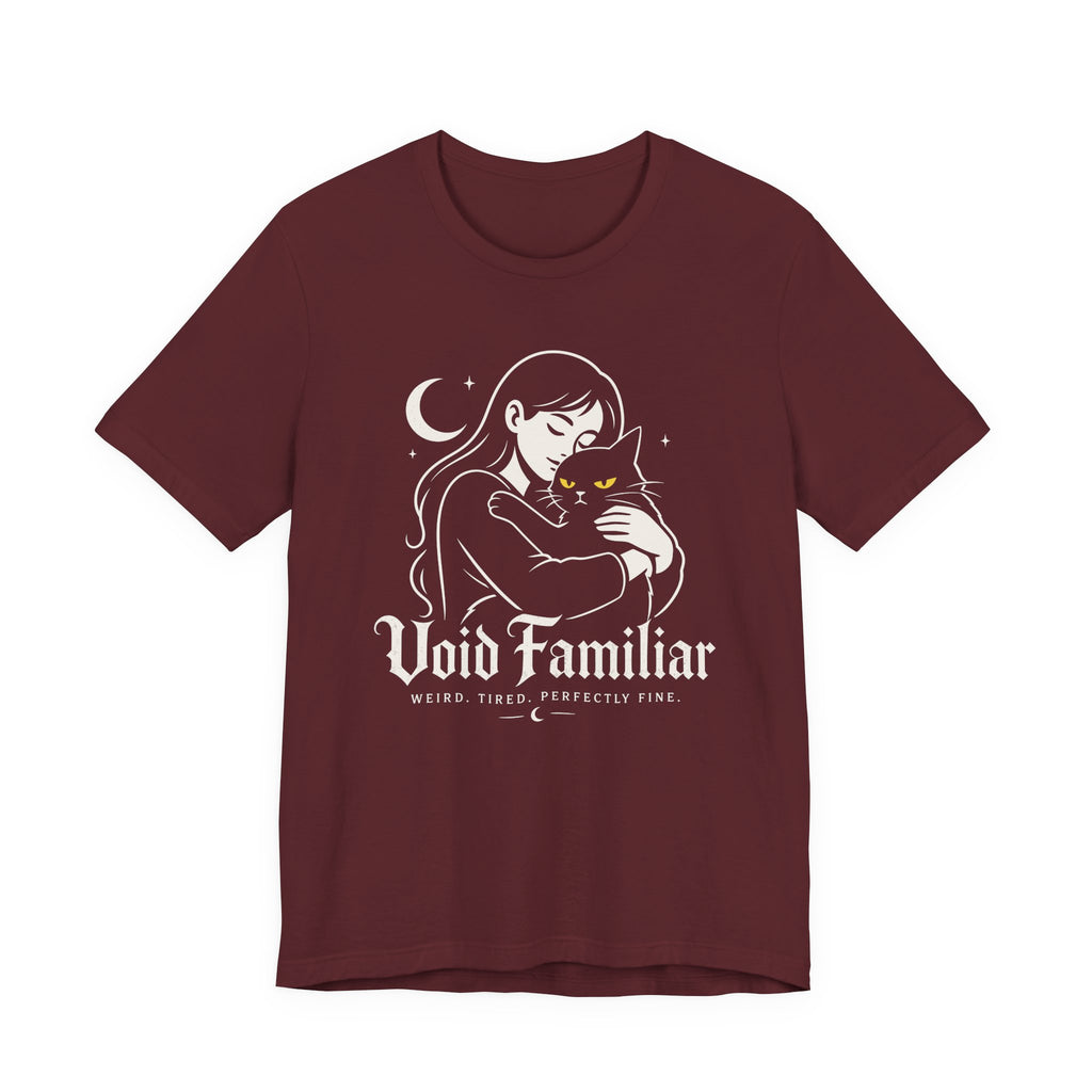 A maroon short-sleeve crewneck t-shirt featuring a graphic with Woman hugging a black cat beneath a crescent moon with “Void Familiar” and “Weird. Tired. Perfectly Fine.” text