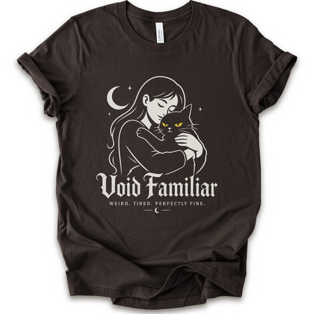 Brown graphic t-shirt with a woman hugging a black cat beneath a crescent moon with “Void Familiar” and “Weird. Tired. Perfectly Fine.” text