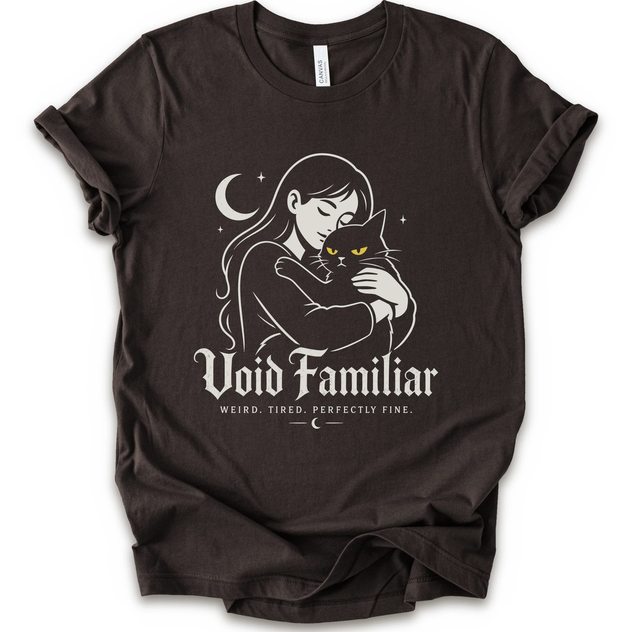 Brown graphic t-shirt with a woman hugging a black cat beneath a crescent moon with “Void Familiar” and “Weird. Tired. Perfectly Fine.” text