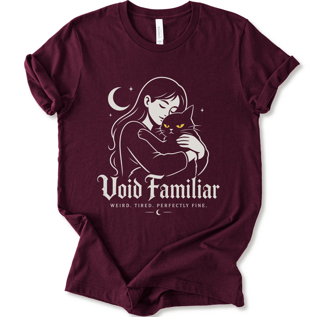 Maroon graphic t-shirt with a woman hugging a black cat beneath a crescent moon with “Void Familiar” and “Weird. Tired. Perfectly Fine.” text