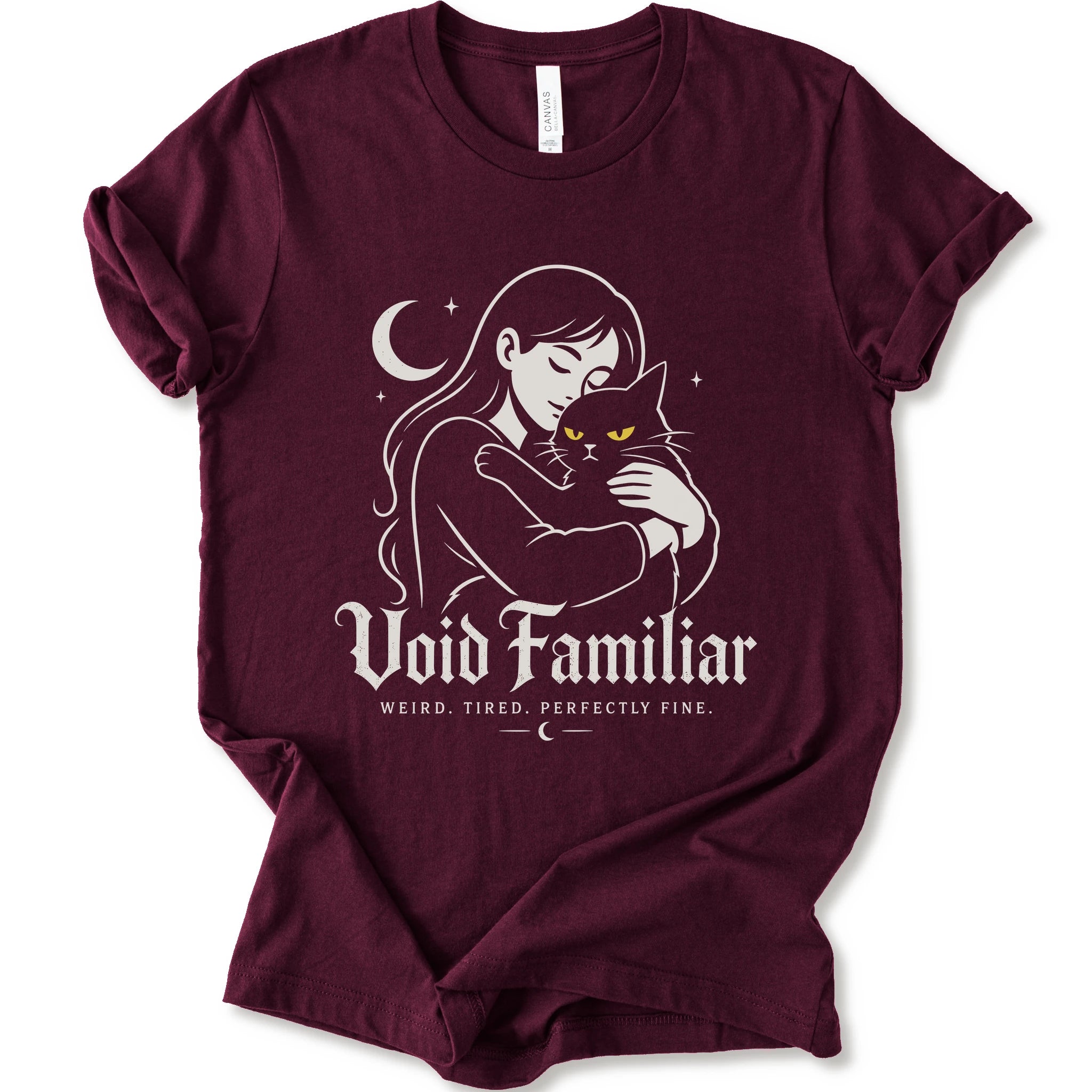 Maroon graphic t-shirt with a woman hugging a black cat beneath a crescent moon with “Void Familiar” and “Weird. Tired. Perfectly Fine.” text