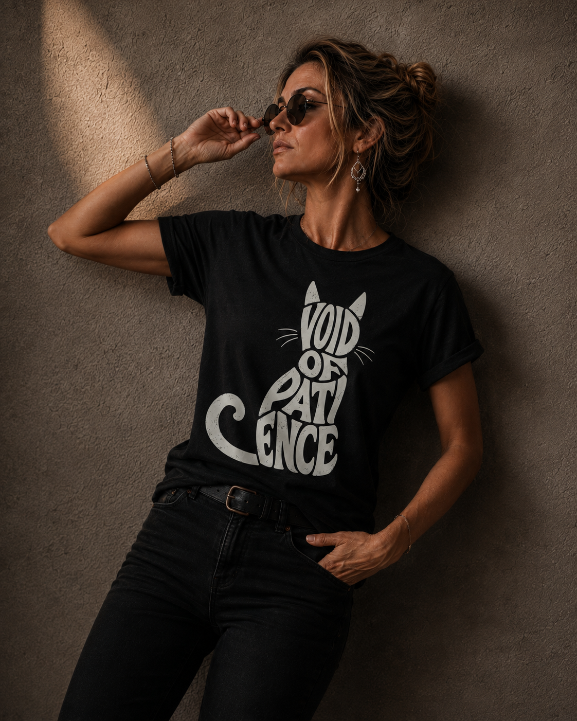 A woman wearing a black graphic t-shirt with a white cat silhouette and the text 'VOID OF PATIENCE' leans against a textured concrete wall.