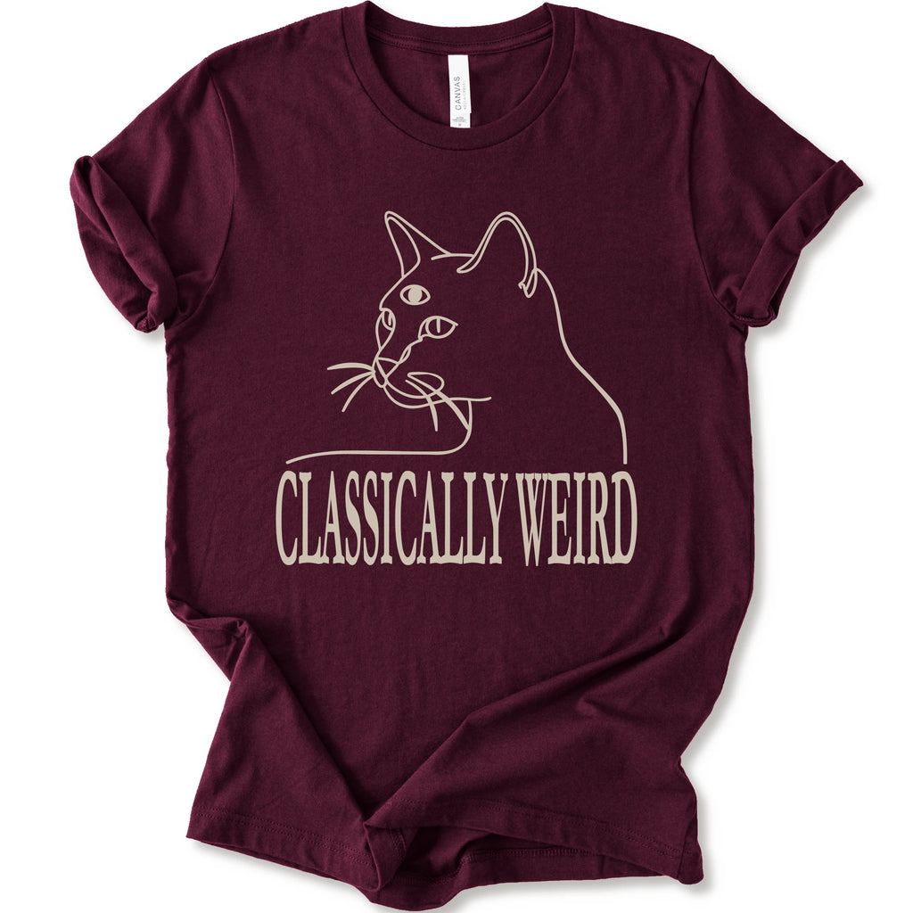 A maroon short-sleeve crewneck t-shirt with a cream-colored graphic of a cat's outline and the text 'CLASSICALLY WEIRD'.