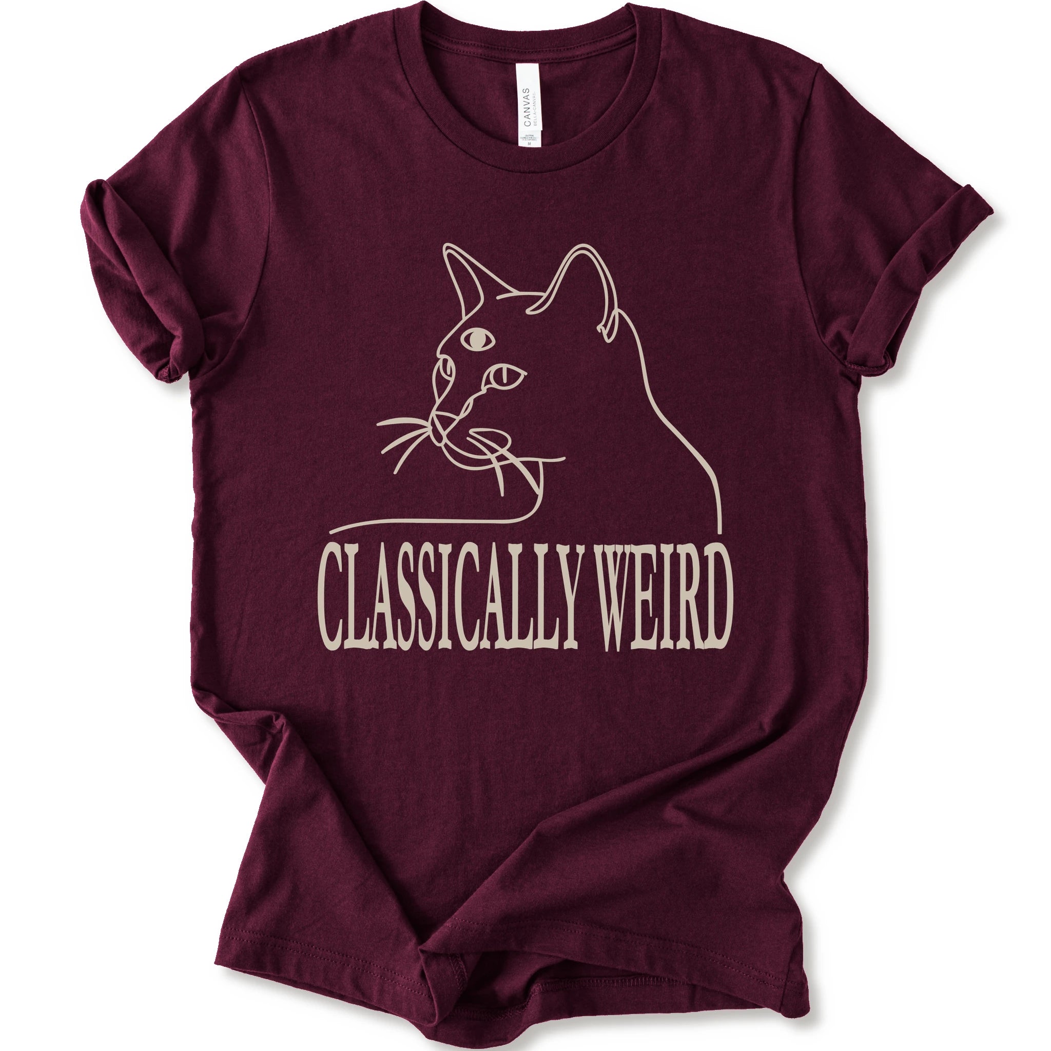 A maroon short-sleeve crewneck t-shirt with a cream-colored graphic of a cat's outline and the text 'CLASSICALLY WEIRD'.