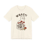 An natural short-sleeve t-shirt with a graphic of a brown cat sitting among red flowers, with the text 'WHAT?!' above it